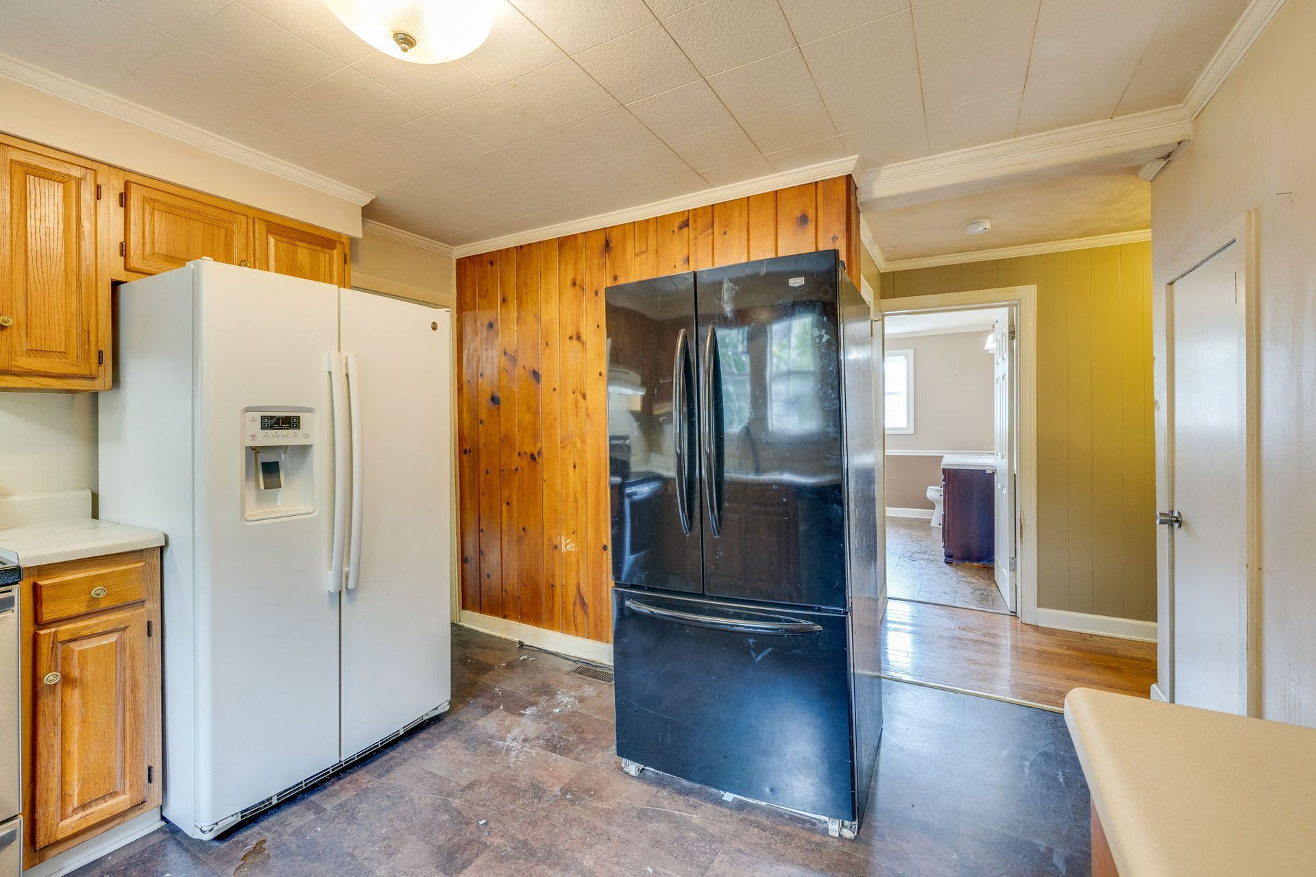 Kitchen with white fridge, black stove, and wood-paneled walls leading to a bright adjoining room