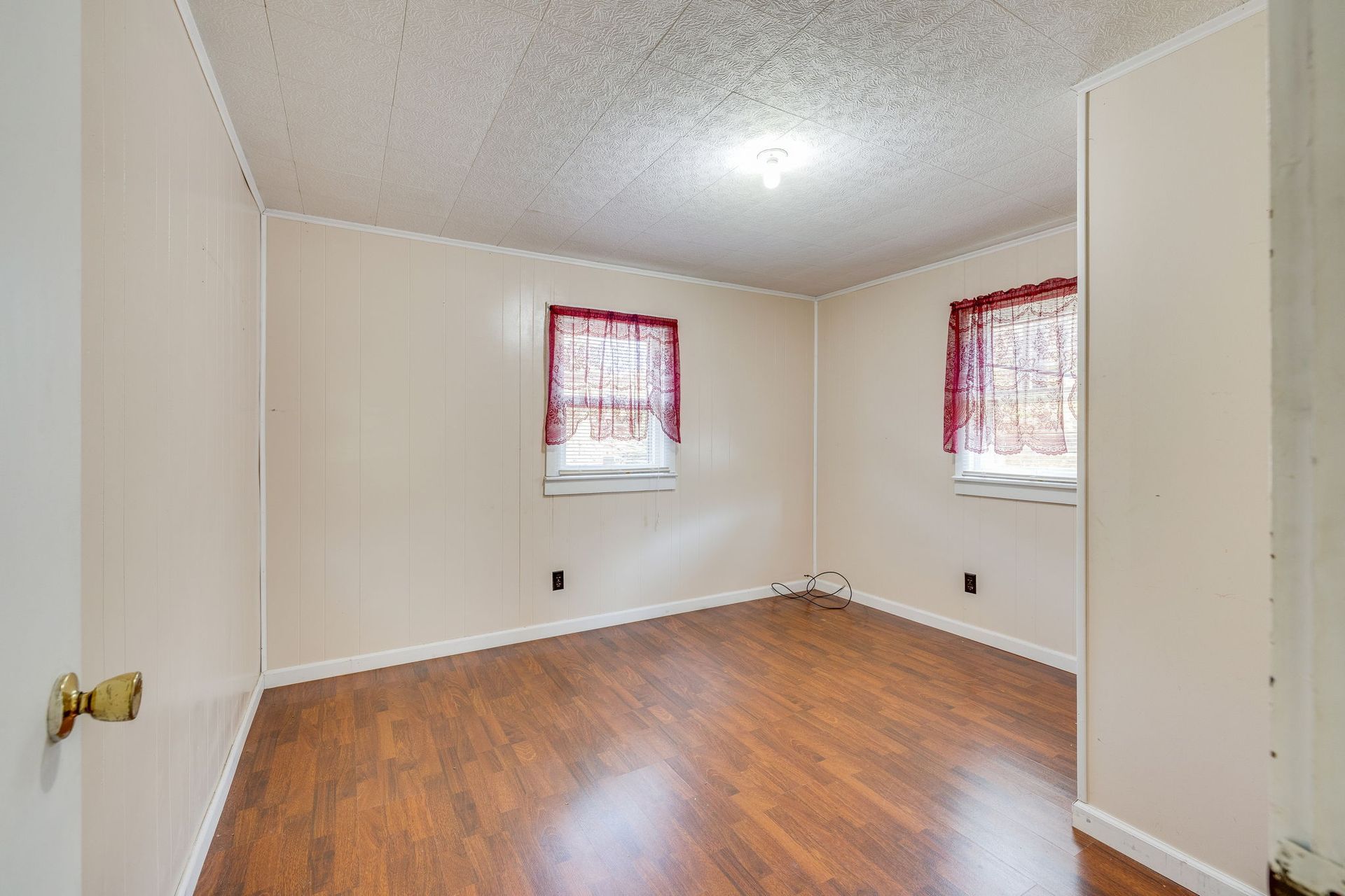 Empty beige room with wood floors and two windows with red curtains