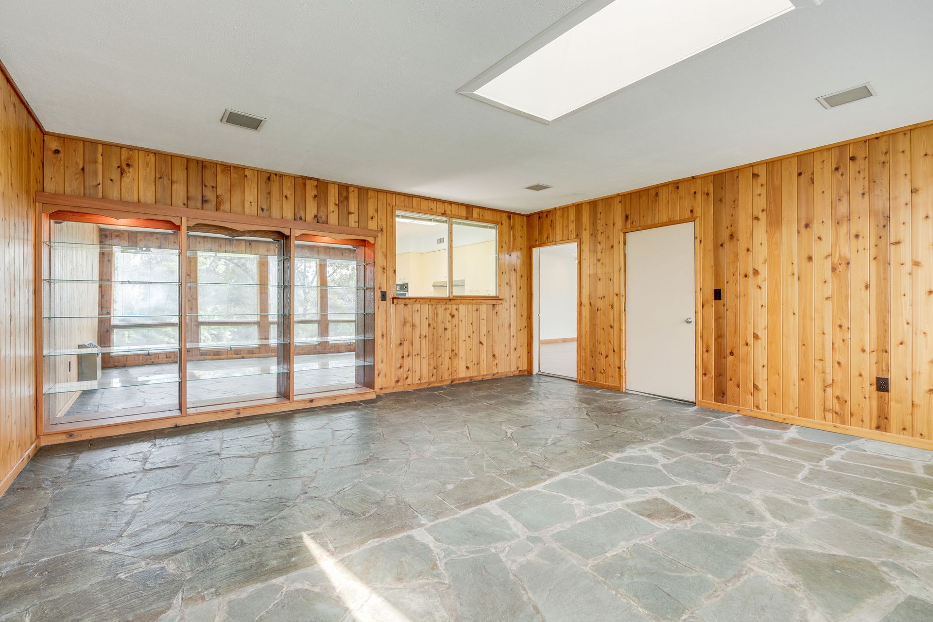 Empty sunroom with wood-paneled walls, stone floor, and large windows letting in bright light