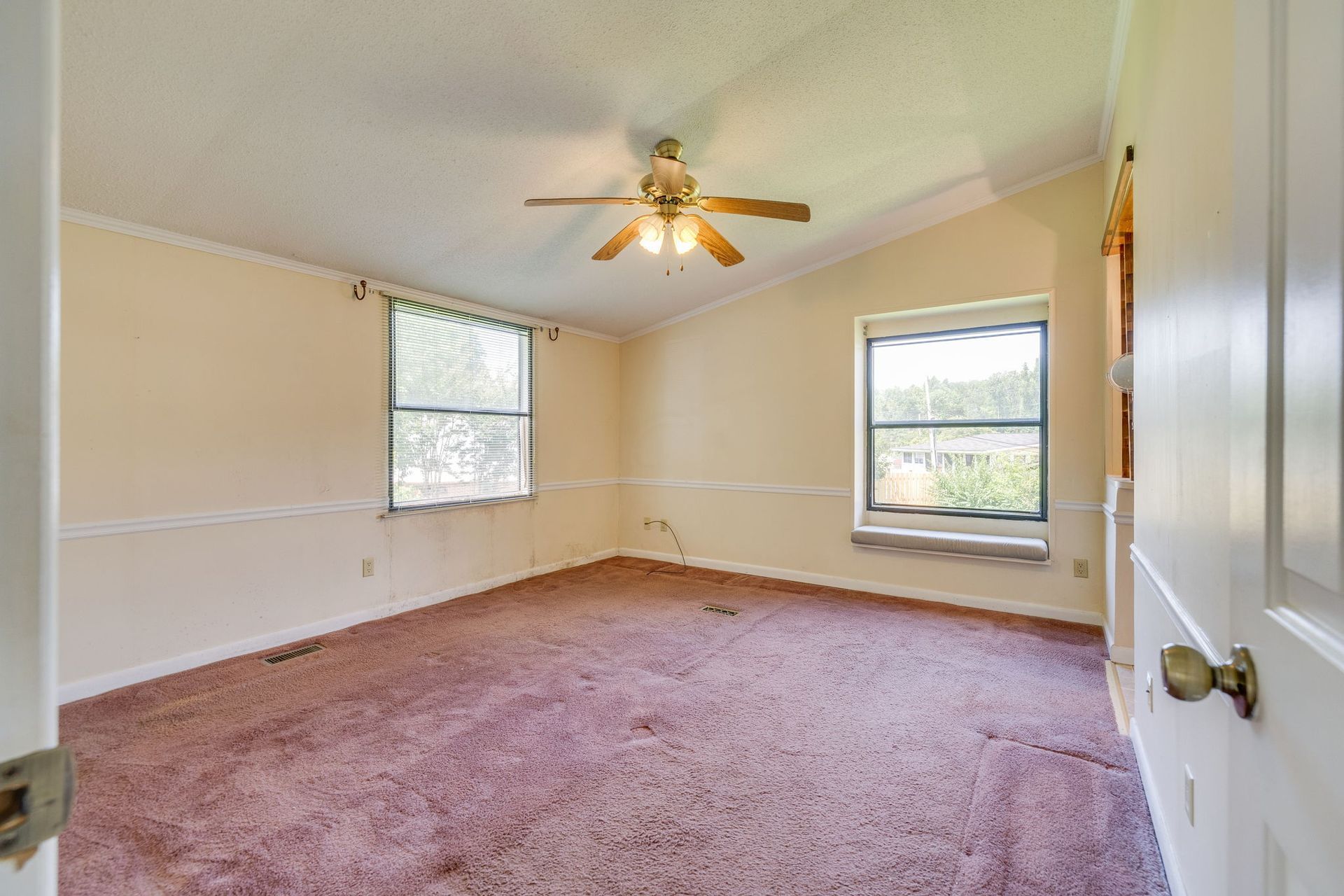 Empty beige bedroom with pink carpet, ceiling fan, and two windows.
