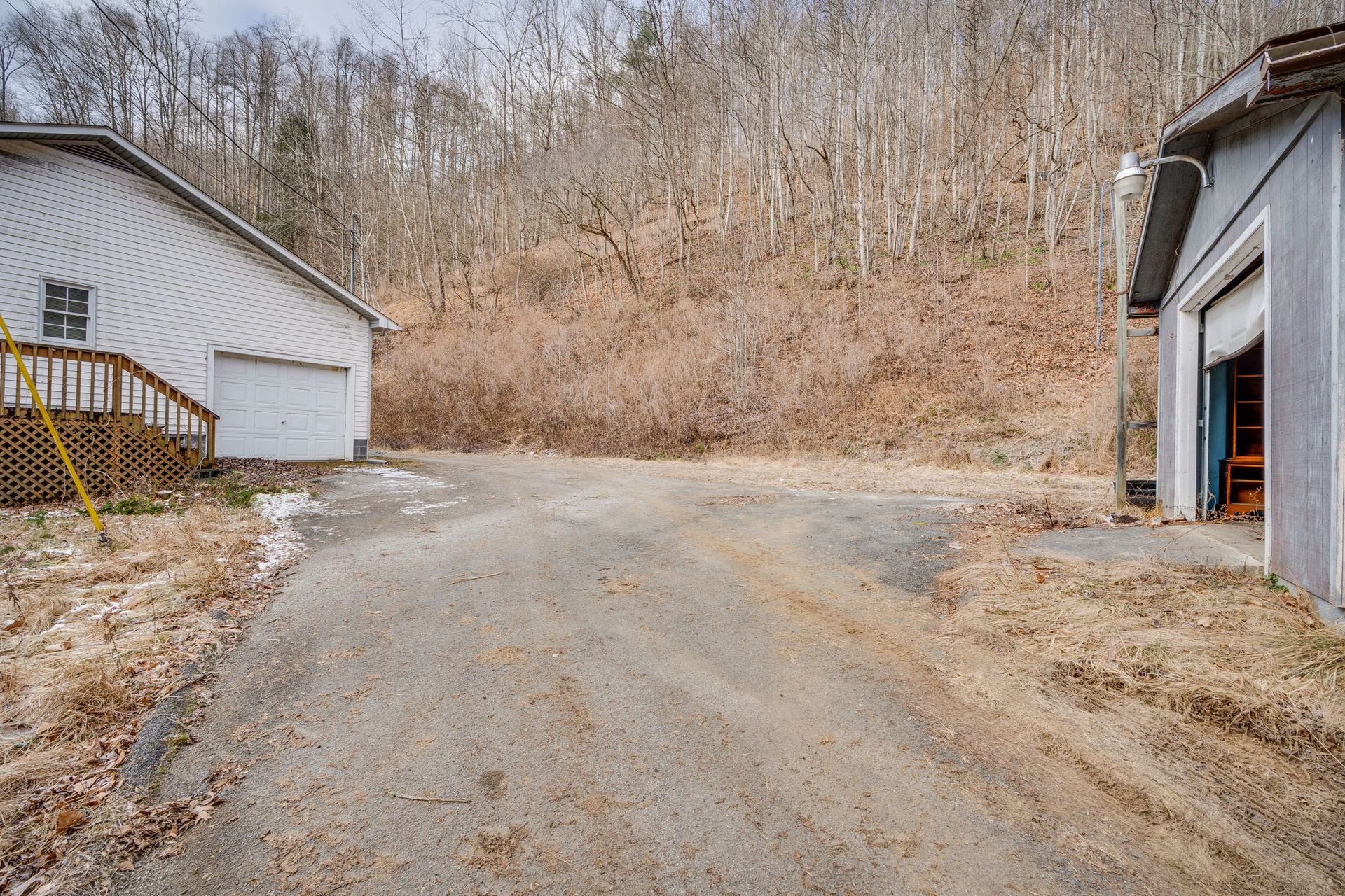 Gravel driveway between two white buildings. Bare trees on a hillside in background.