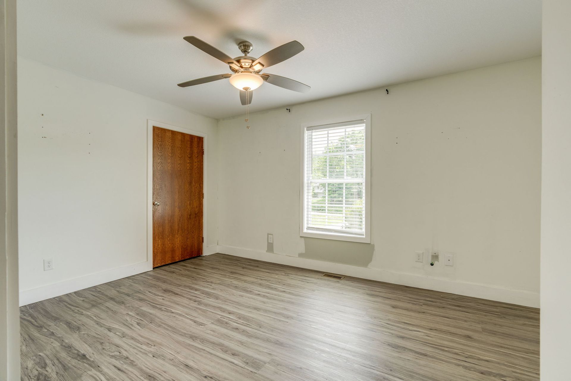 Empty bedroom with wood-look flooring, white walls, a ceiling fan, window, and closed closet door