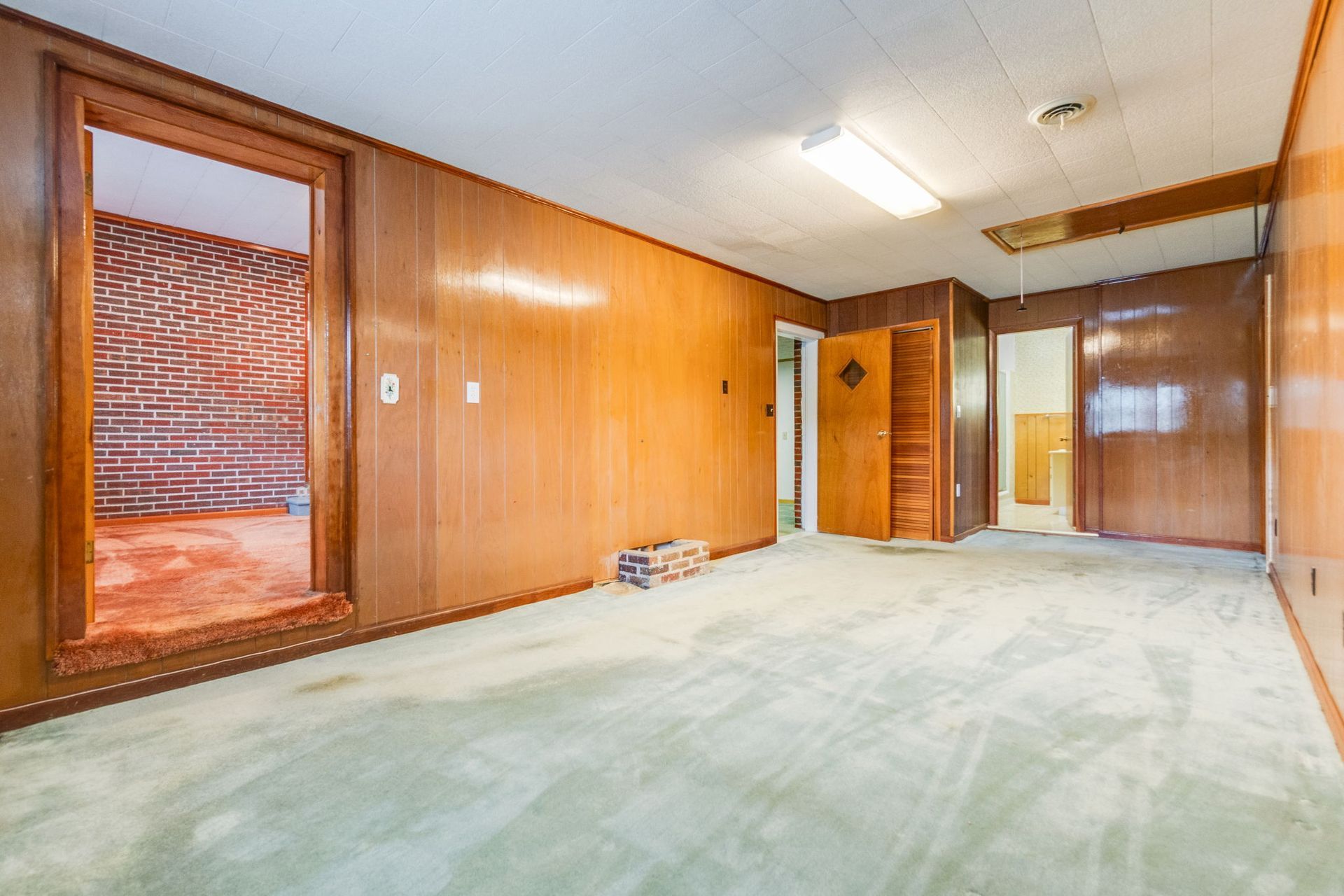 Empty wood-paneled room with green carpet, ceiling lights, and open doorways