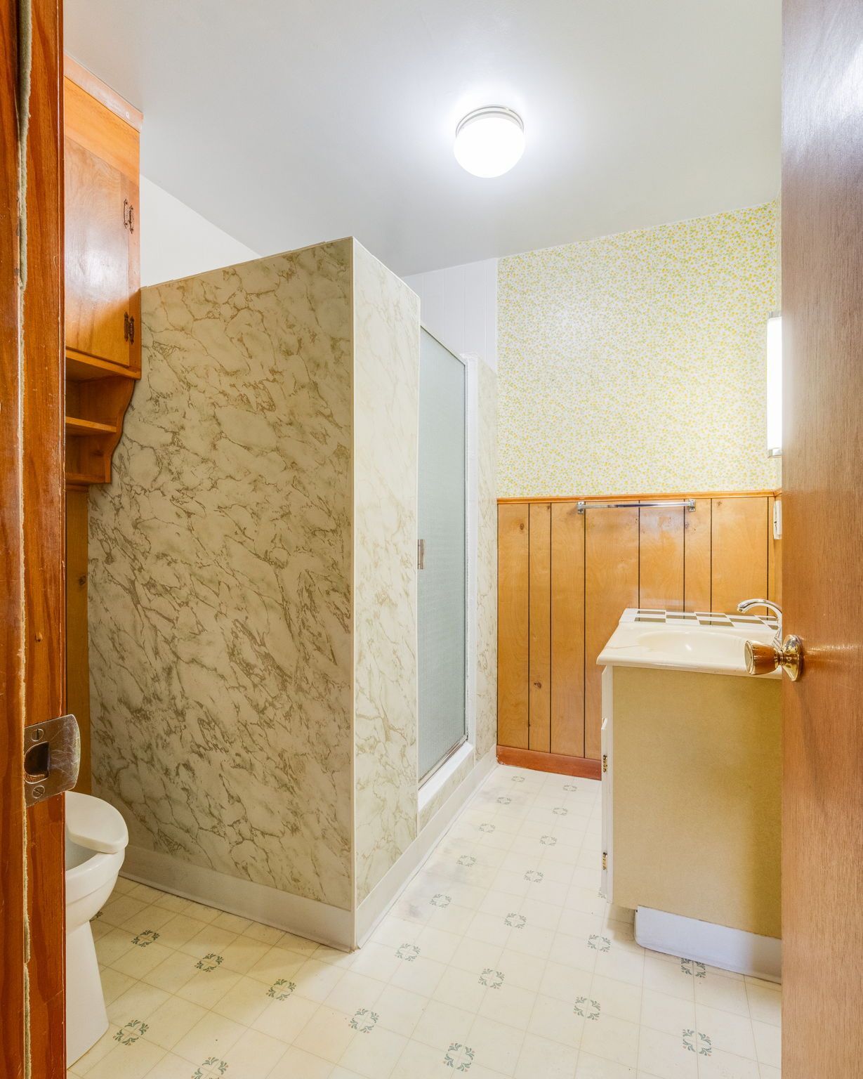 Narrow bathroom with tiled floor, shower stall, wood paneling, and a sink under a bright ceiling light