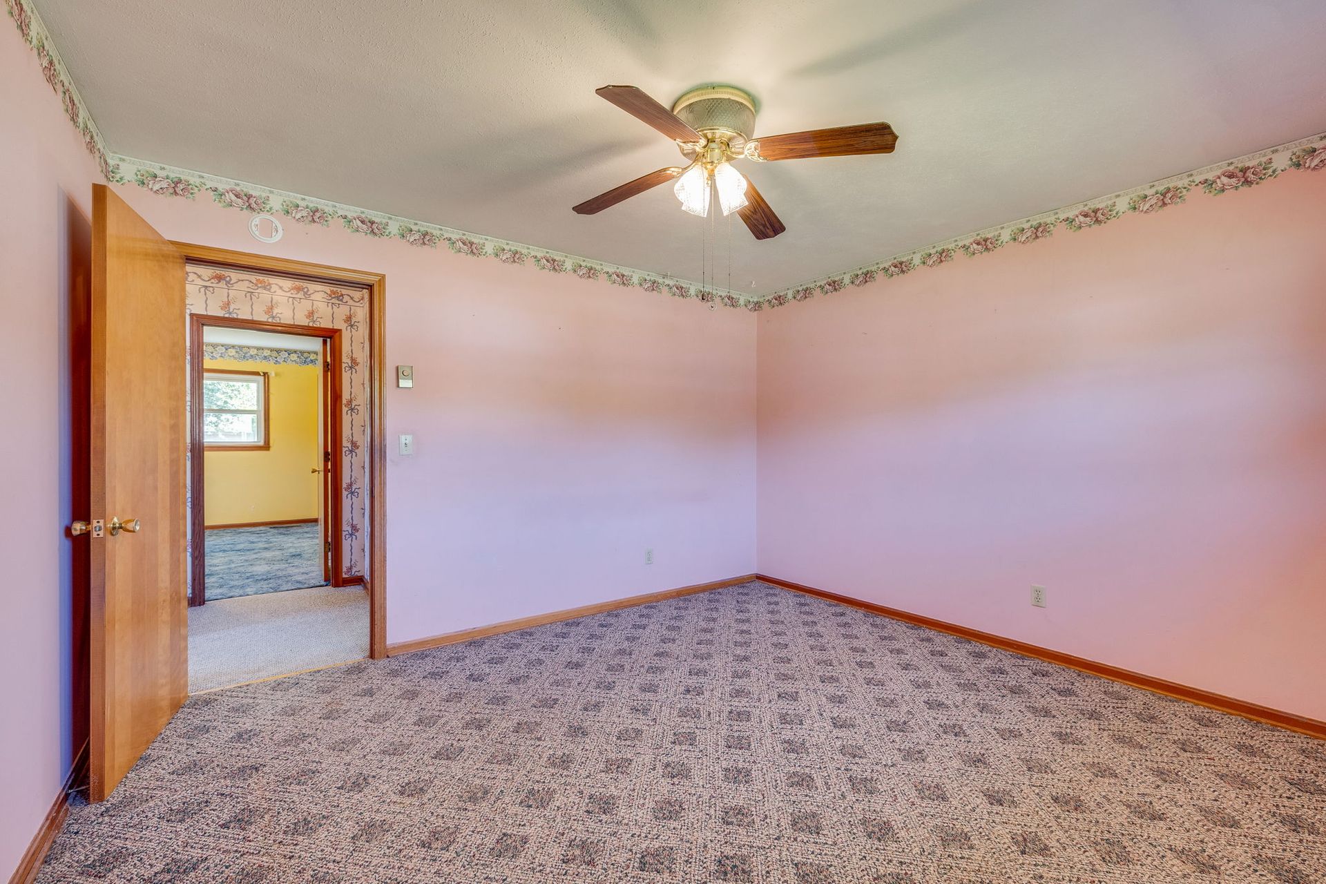 Empty bedroom with pink walls, patterned carpet, and a ceiling fan
