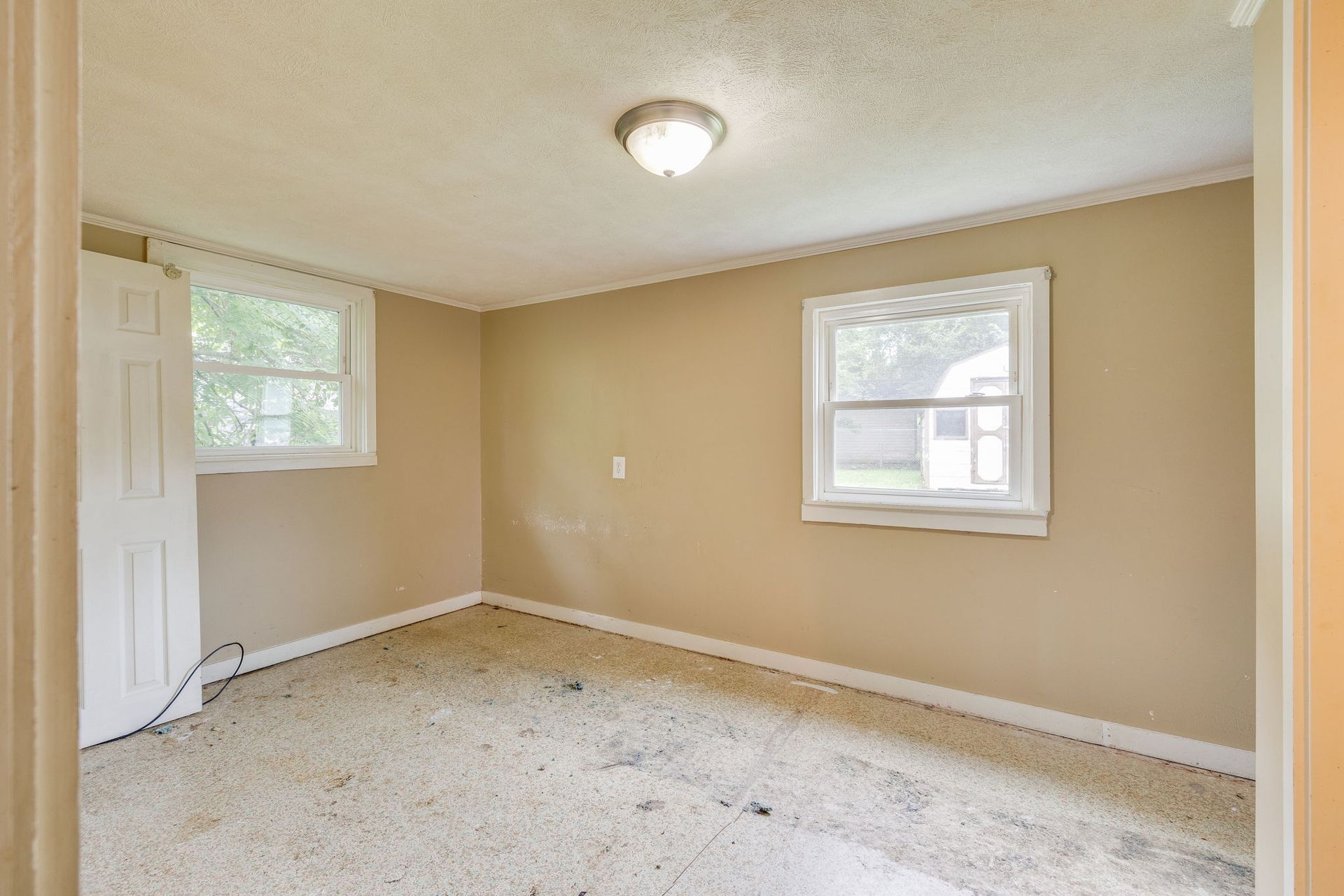 Empty beige bedroom with two windows, white trim, carpeted floor, and ceiling light.