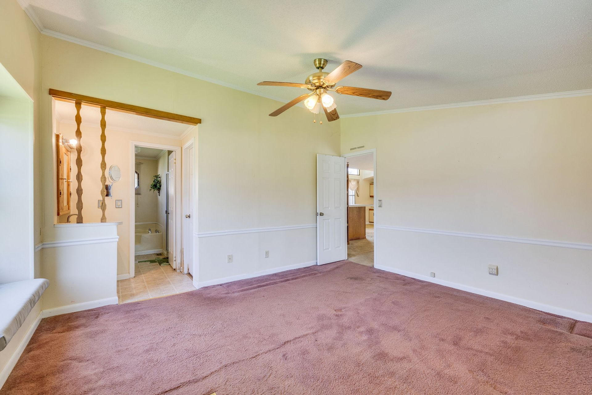 Empty bedroom with pink carpet, white walls, ceiling fan, and open doorways