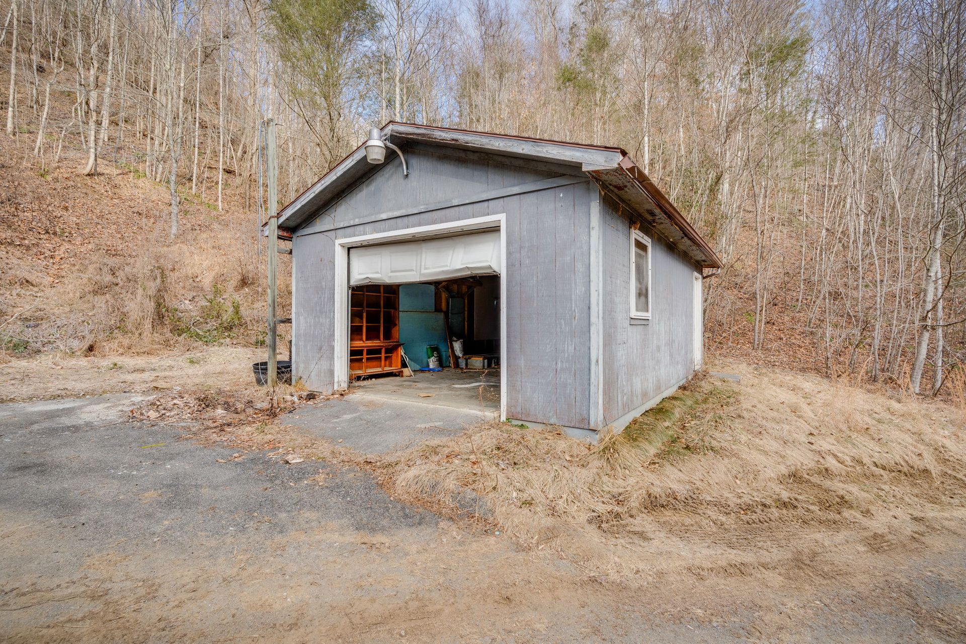 Gray garage with an open door on a hillside.