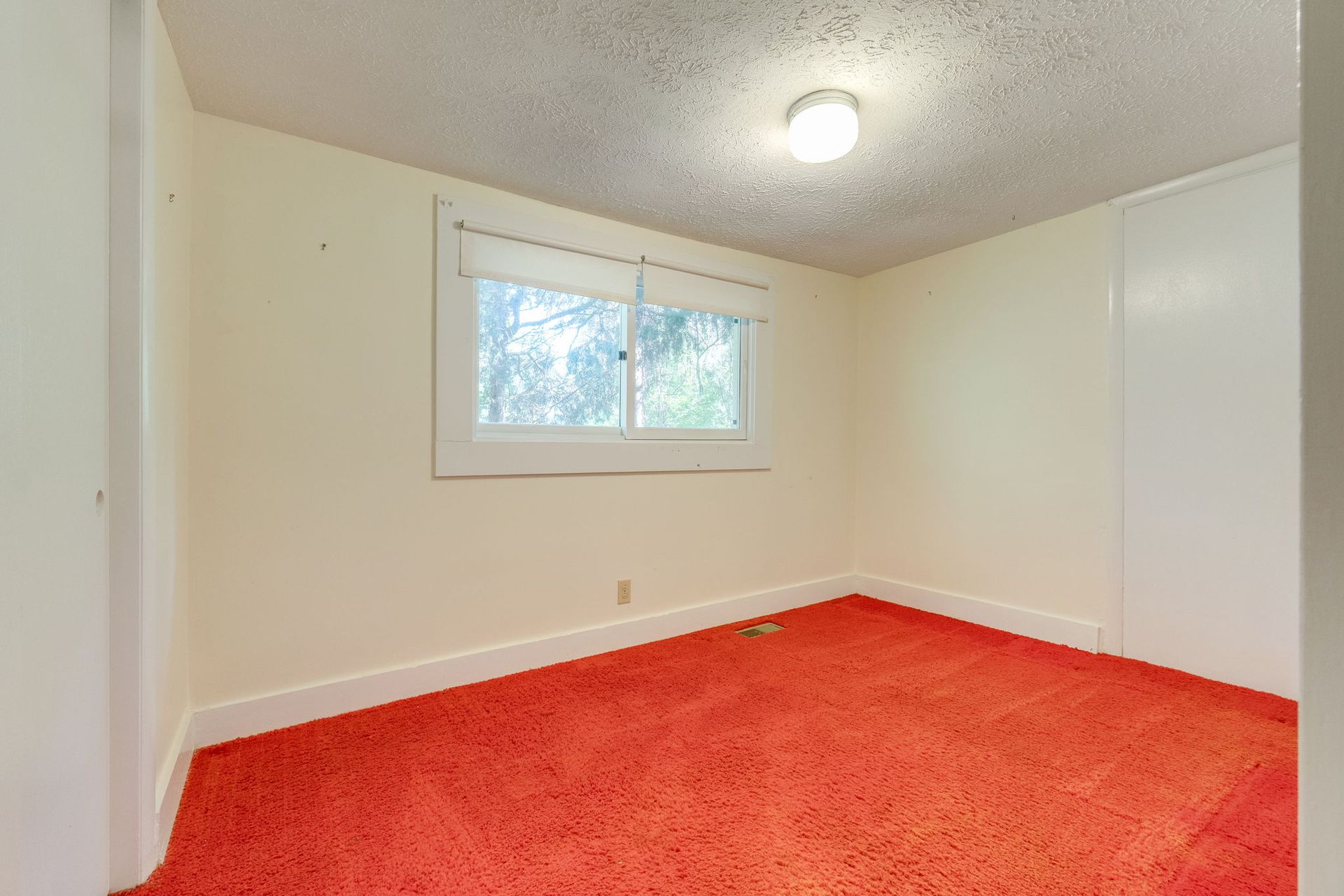 Empty room with bright red carpet, cream walls, a window, and ceiling light