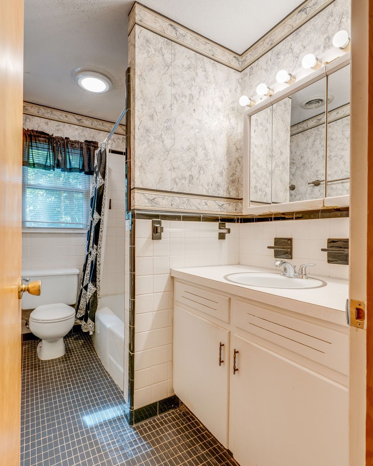 Compact bathroom with vanity, mirror lights, toilet, and shower curtain; white tile and dark floor.