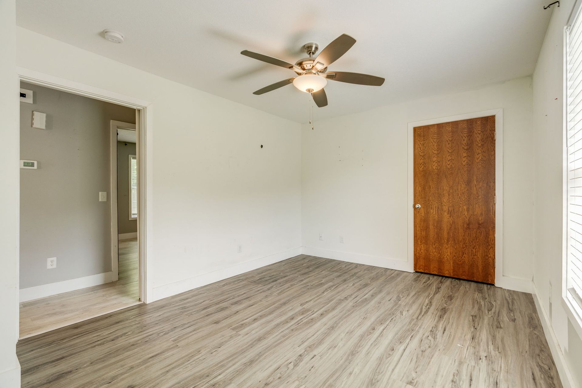 Empty beige bedroom with ceiling fan, wood-look floor, closet door, and window blinds