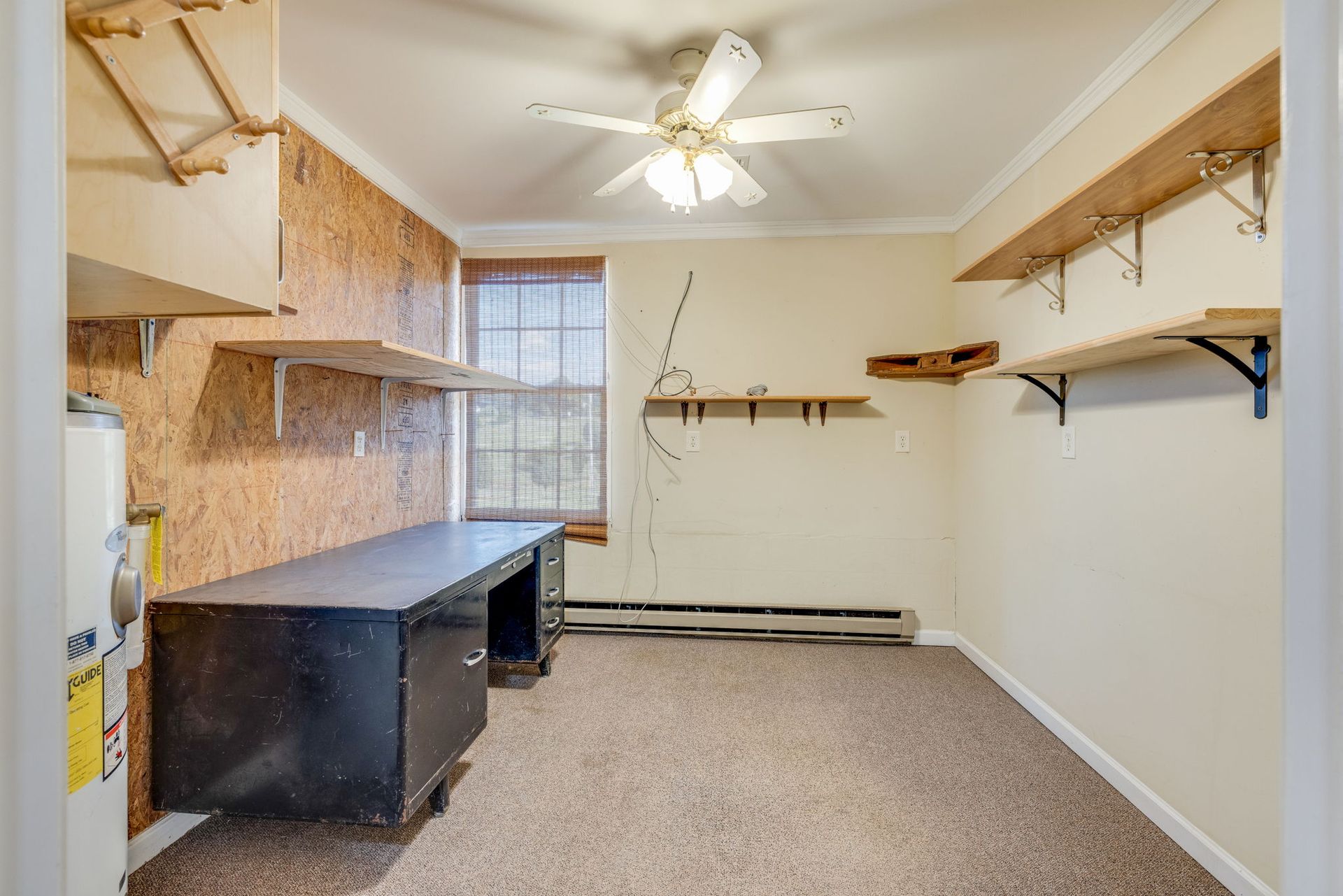 Small empty utility room with shelves, workbenches, carpet, and a ceiling fan.