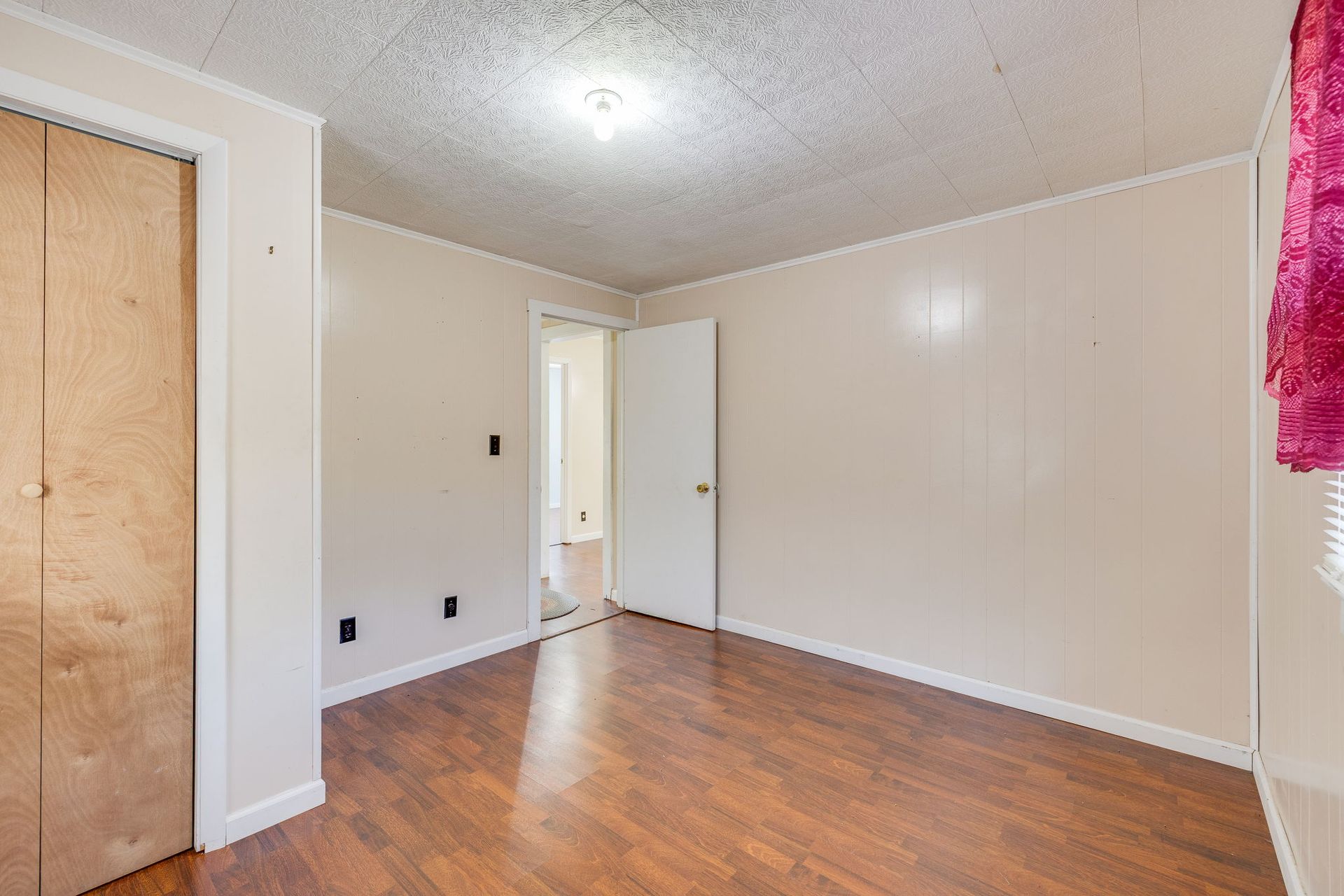 Empty beige room with wood floor, white door, and boarded-up closet opening