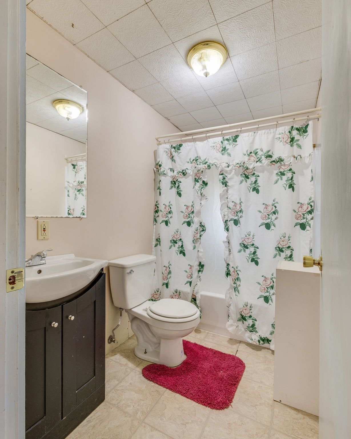 Small bathroom with toilet, sink, floral shower curtain, and pink bath mat.