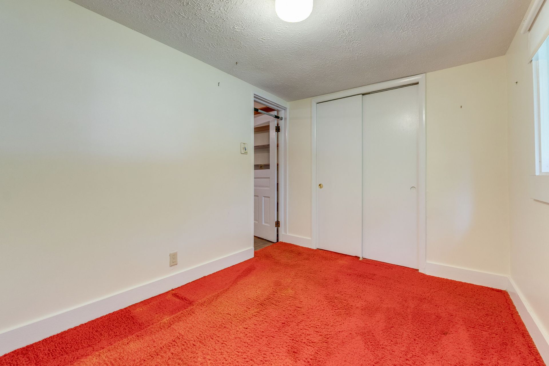 Empty room with bright red carpet, white walls, closet doors, and a ceiling light