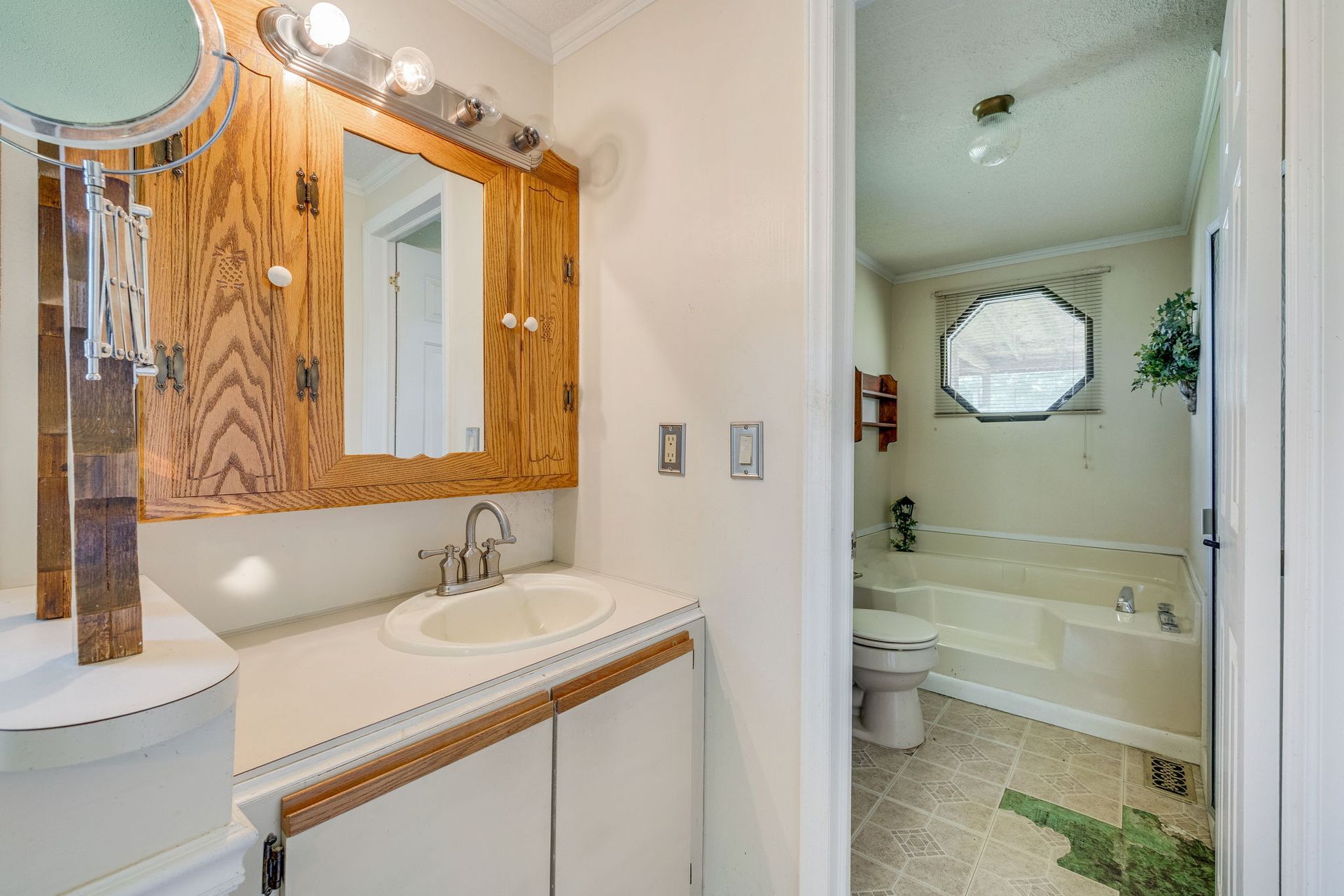 Bathroom vanity with wood-framed mirror and adjoining toilet room, lit by vanity lights.