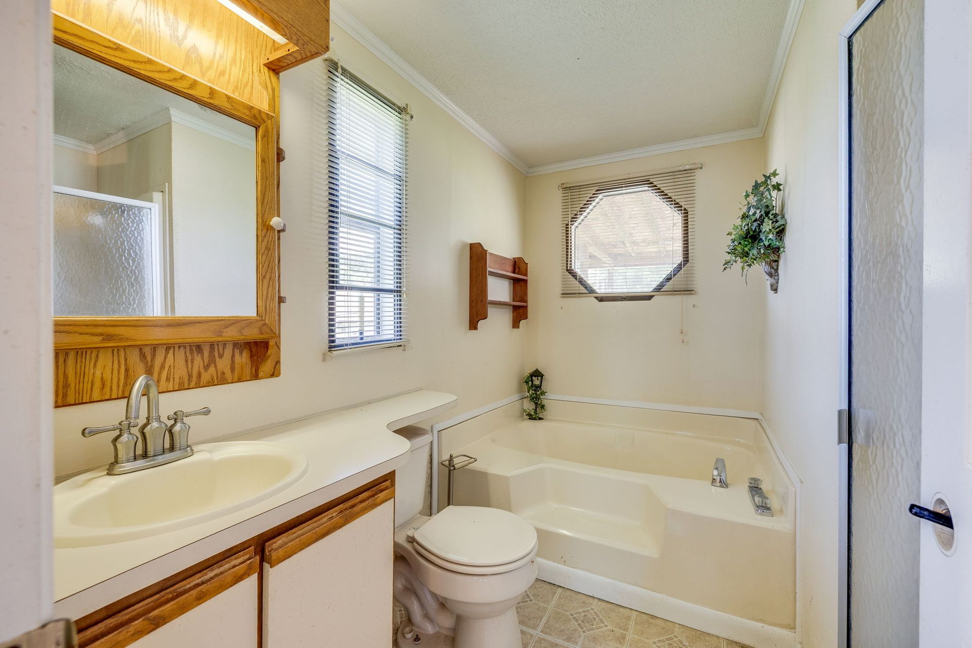 Small bathroom with a vanity, toilet, tub, and octagonal window in soft neutral tones