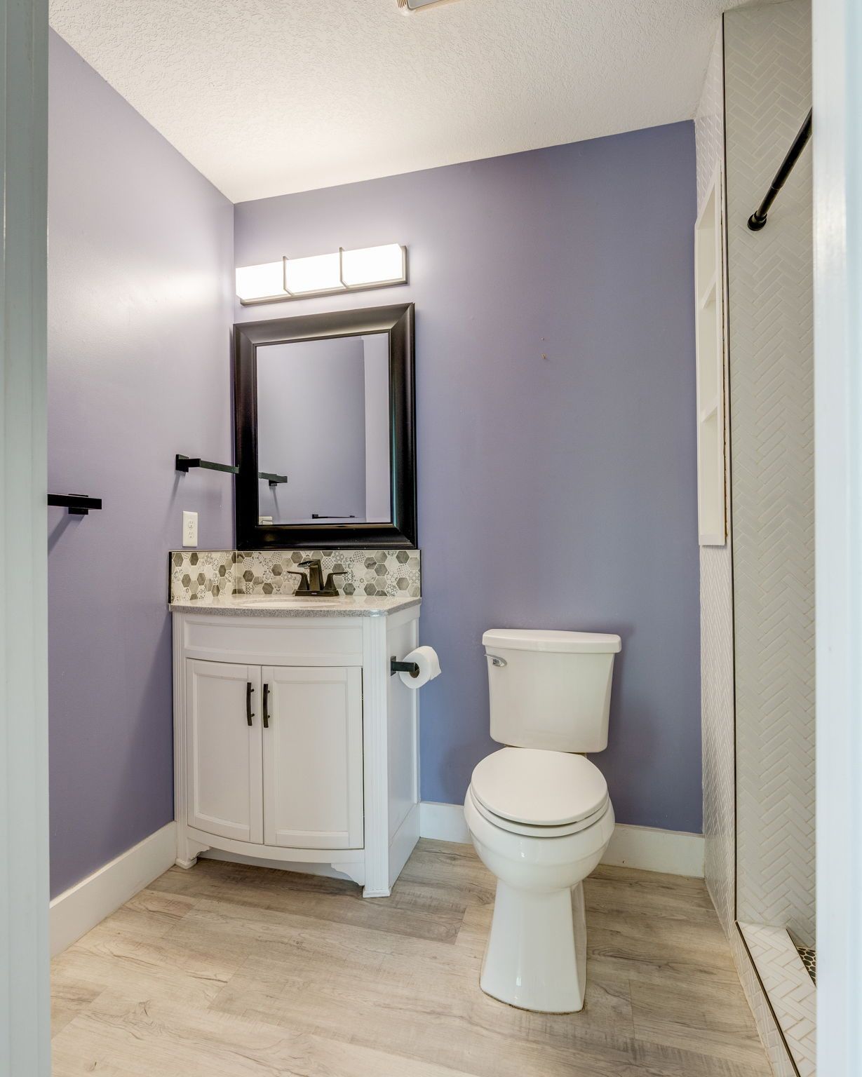 Small bathroom with lavender walls, white vanity and toilet, and a glass shower stall.
