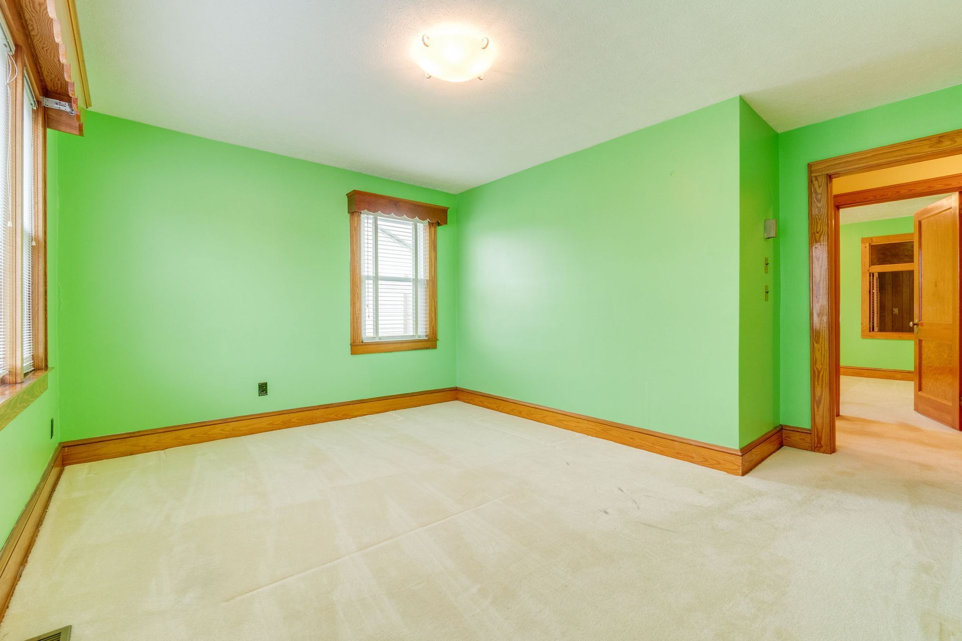 Empty mint-green room with white carpet, wood trim, and a doorway to a lit hallway