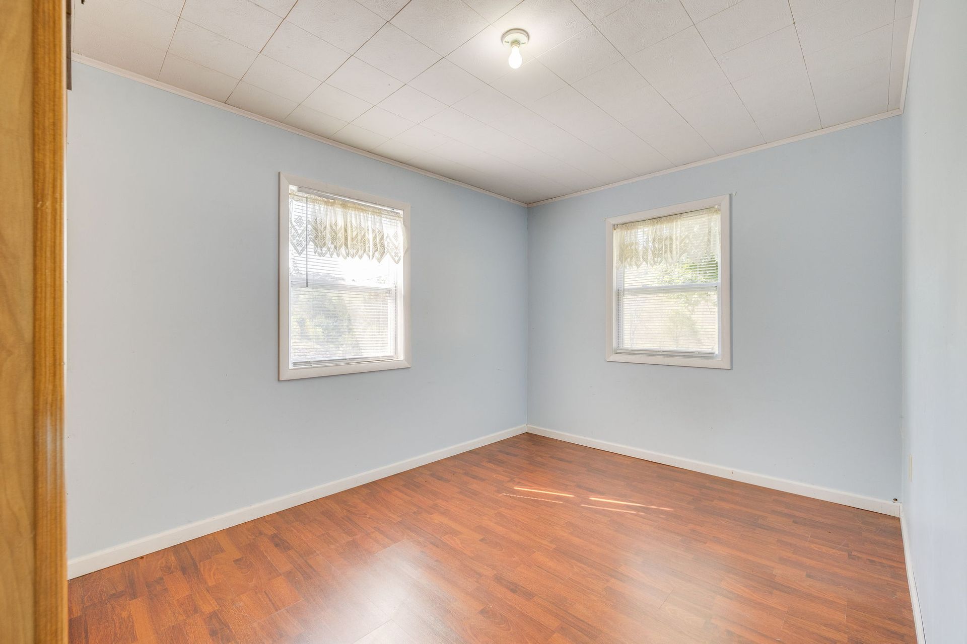 Empty room with light blue walls, hardwood floor, and two small windows with blinds