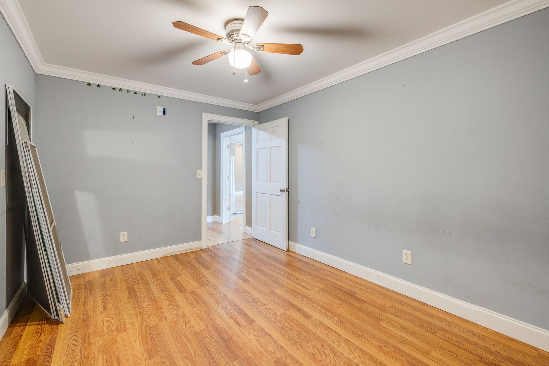 Empty gray bedroom with hardwood floors, ceiling fan, and open doorway to a hall