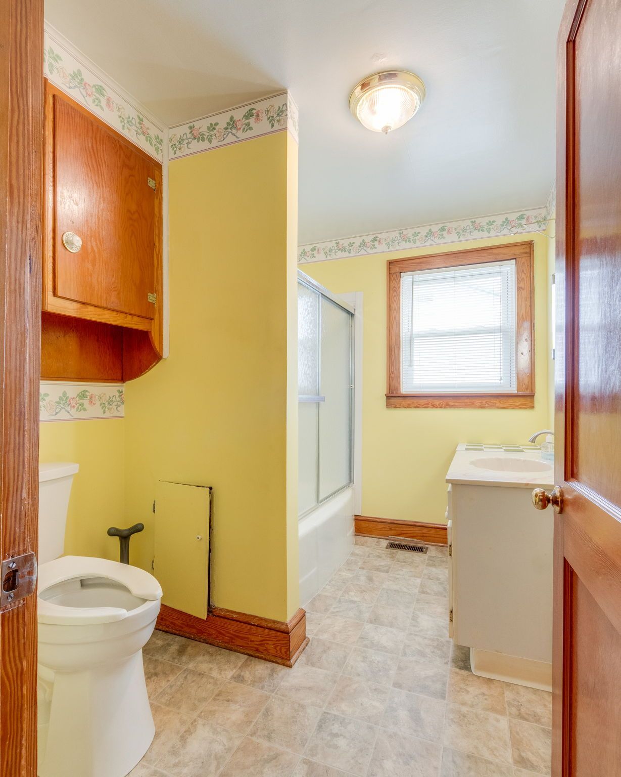 Small yellow bathroom with toilet, bathtub, sink, and wood trim, seen from the doorway