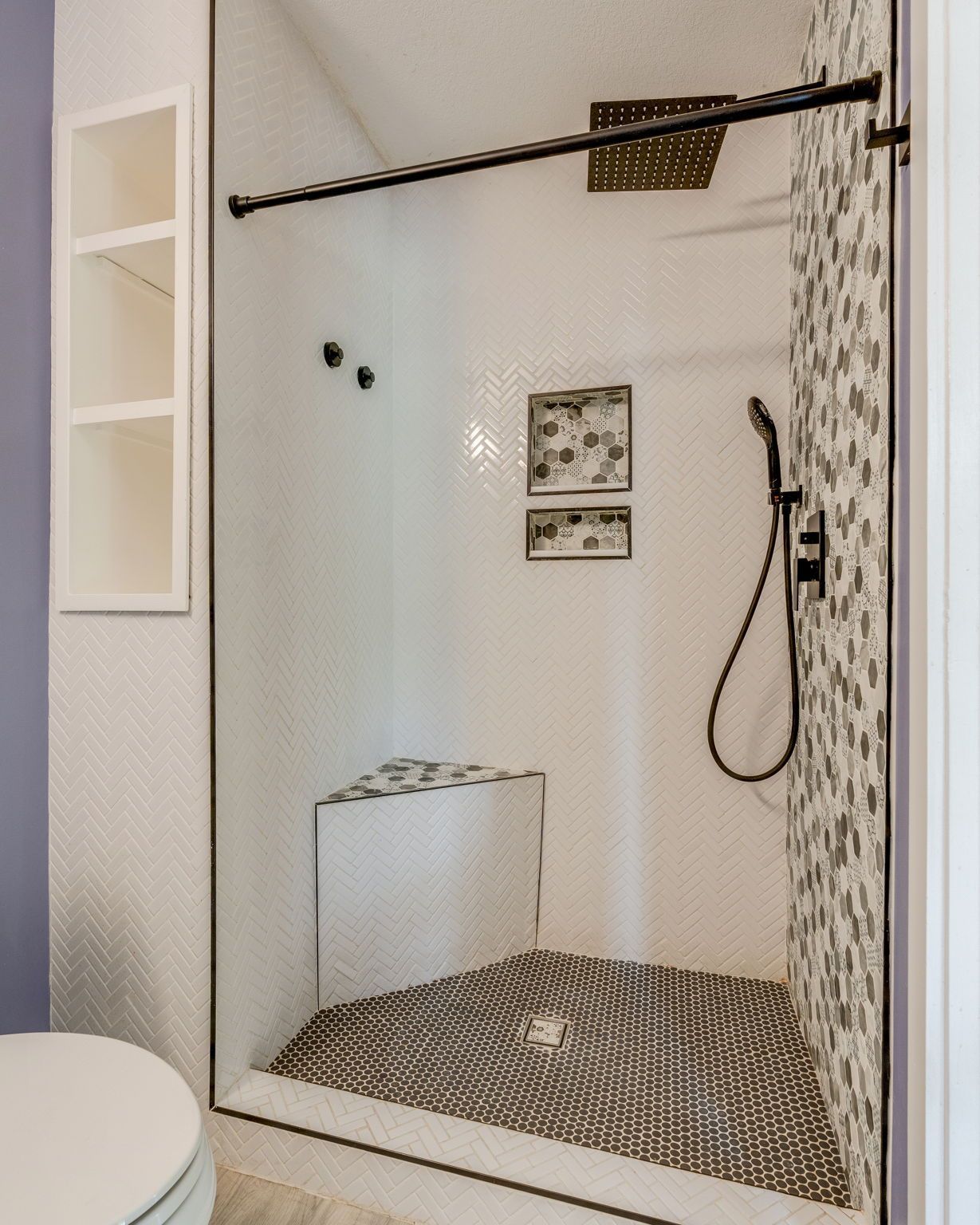 Small bathroom shower with patterned tile floor, wall-mounted showerhead, and hanging handheld sprayer.