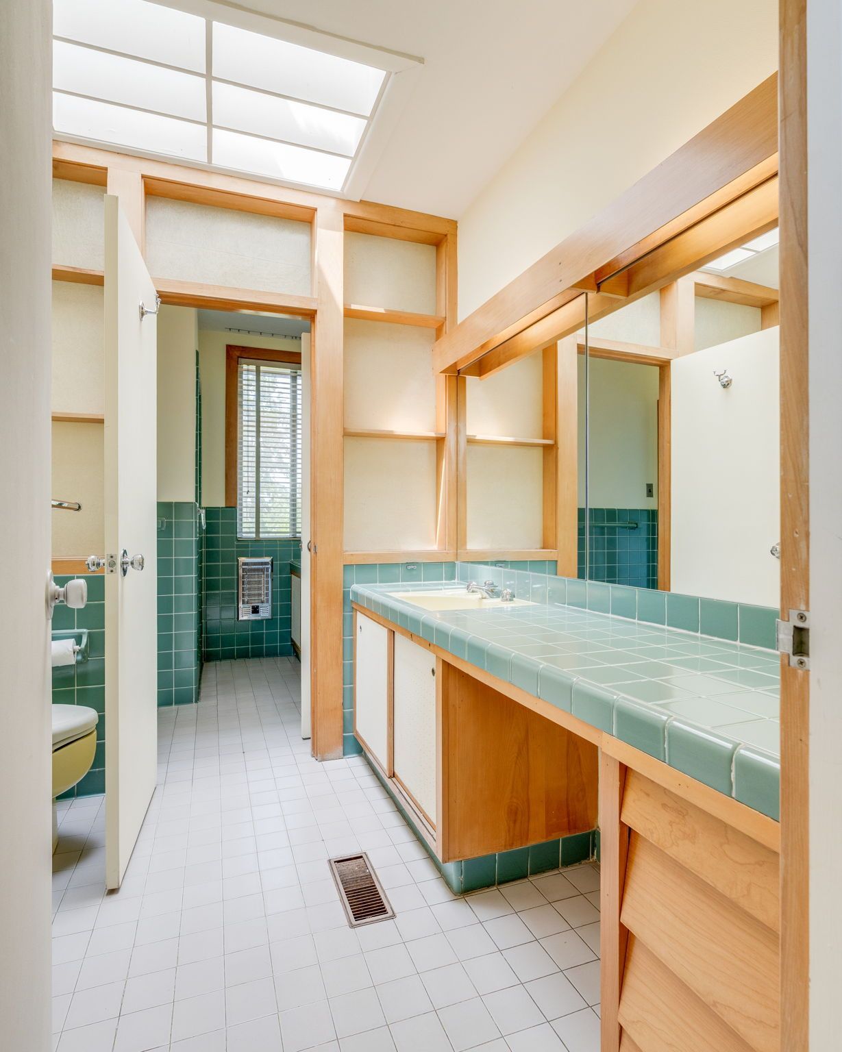Modern bathroom with teal tile counters, wood trim, large mirror, and skylight