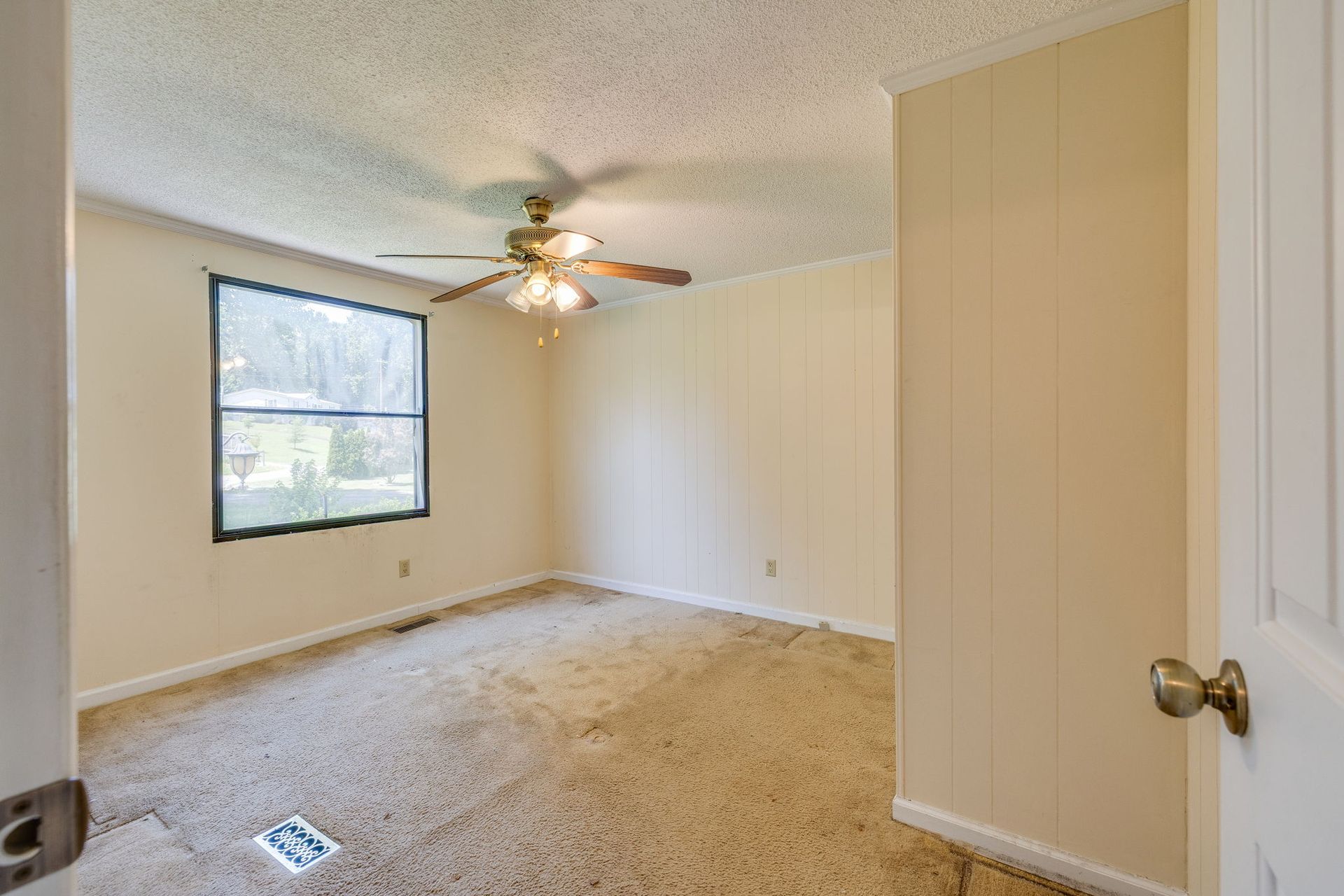 Empty beige bedroom with carpet, window, ceiling fan, and open door