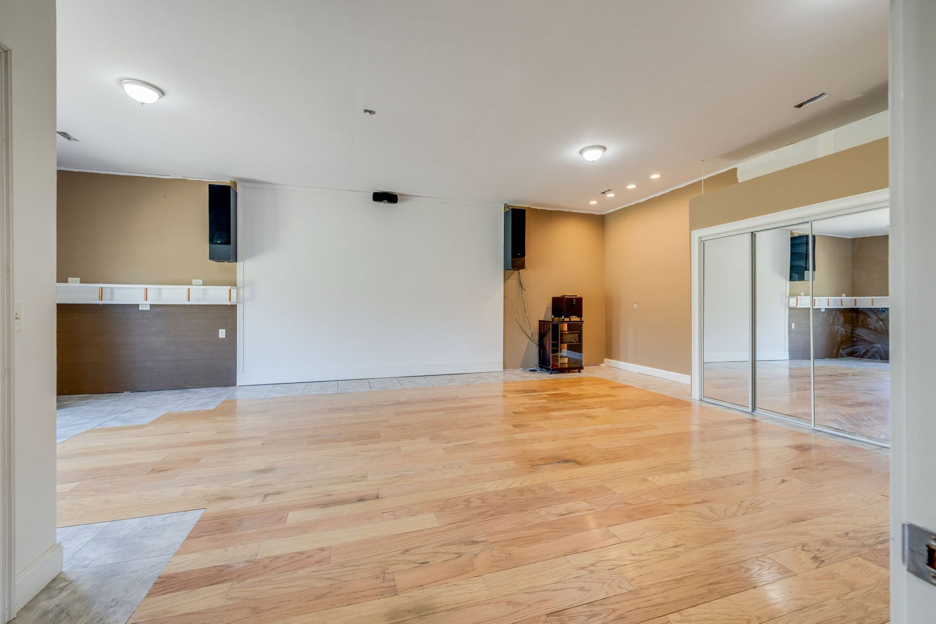 Empty open-plan living room with hardwood floors, beige walls, and a mirrored closet on the right.