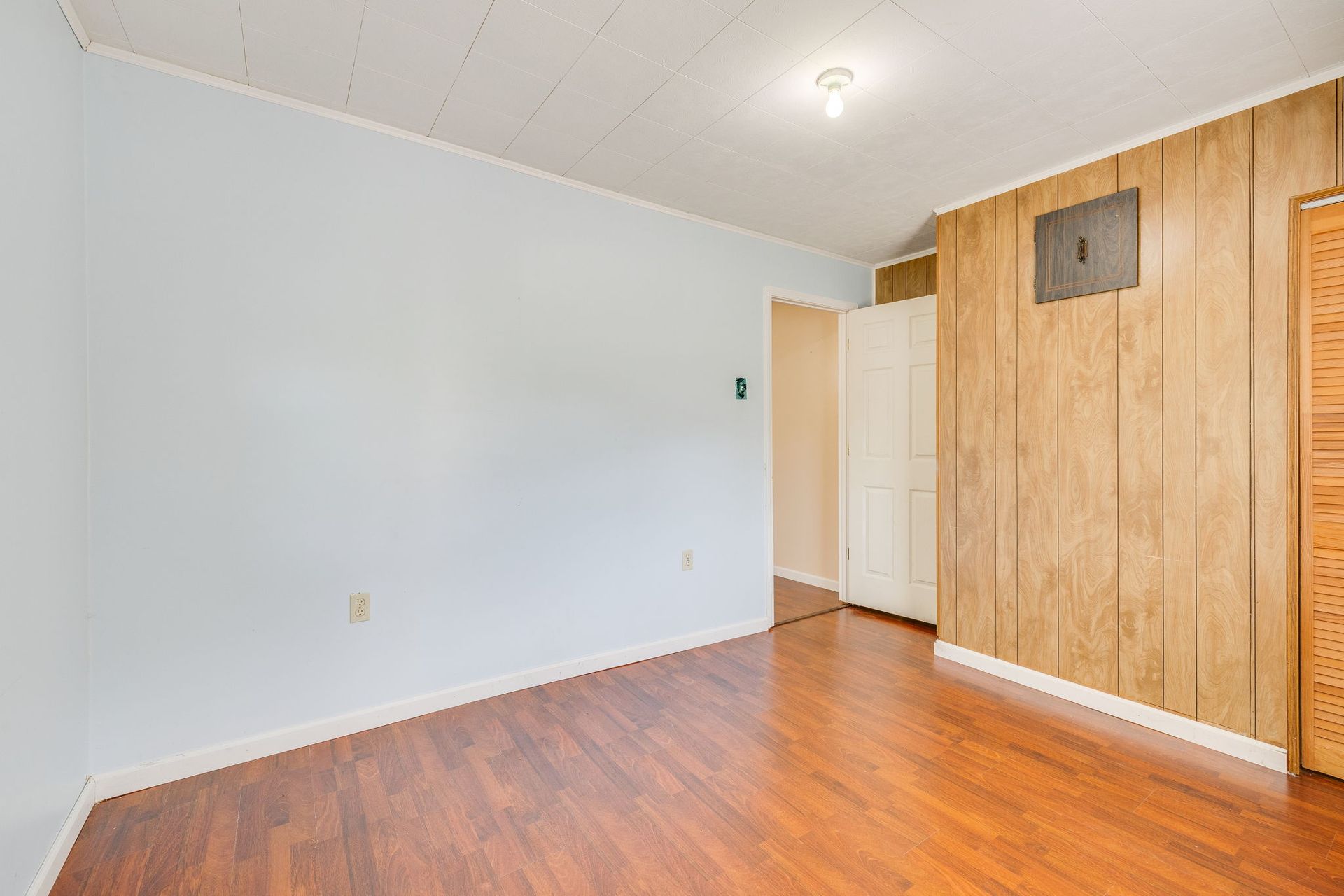 Empty room with light blue walls, wood floor, and built-in wooden closet doors