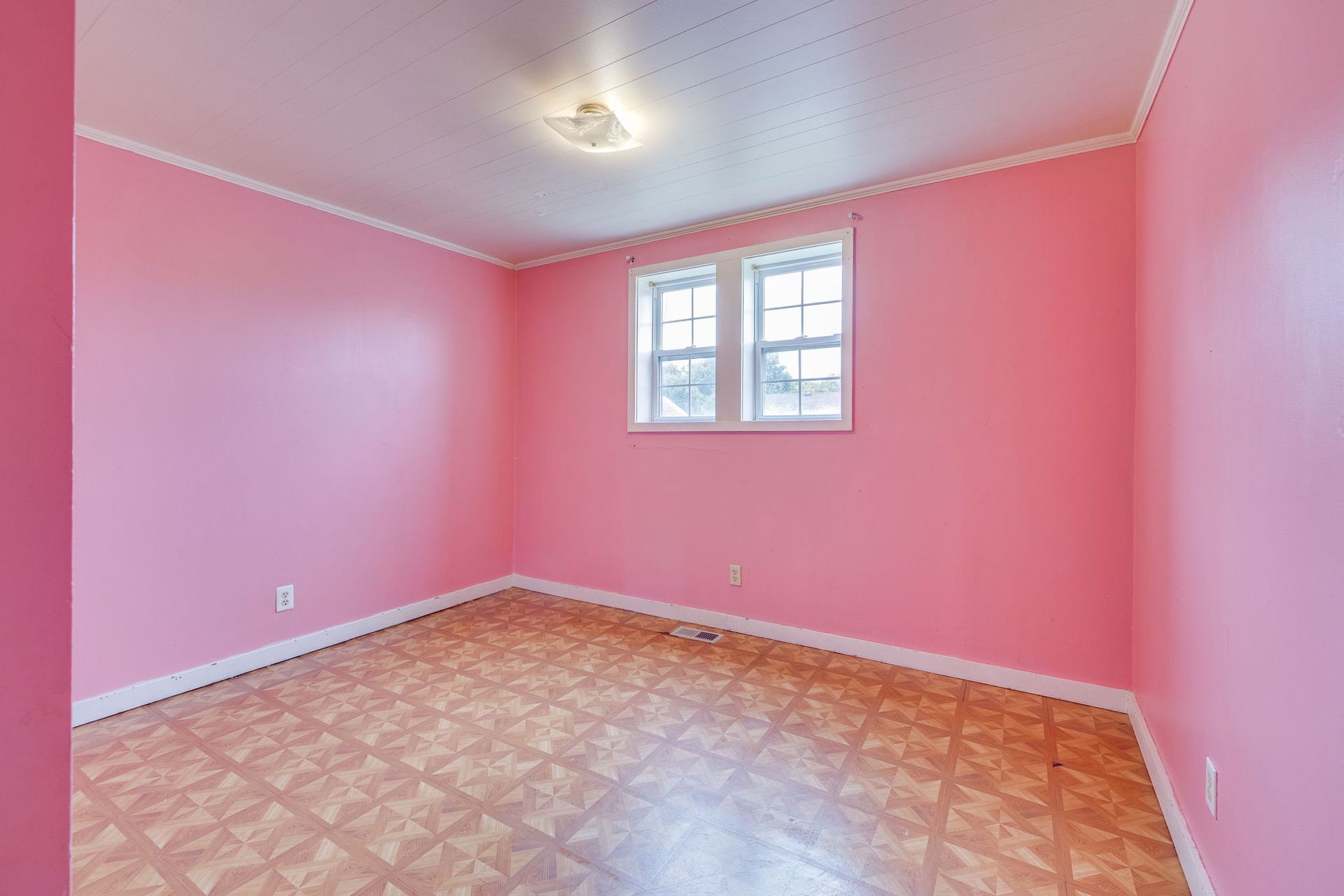Empty pink bedroom with patterned floor and a small window.