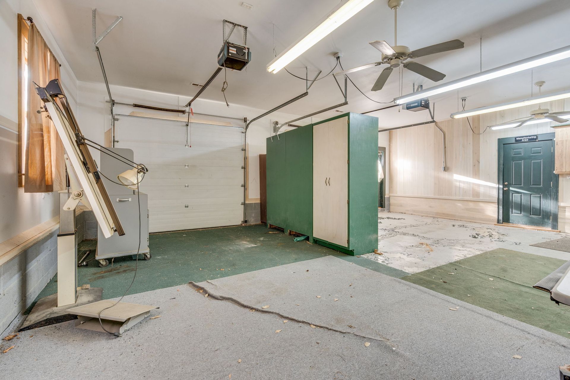Dilapidated garage interior with cracked floor, storage cabinets, and open door.