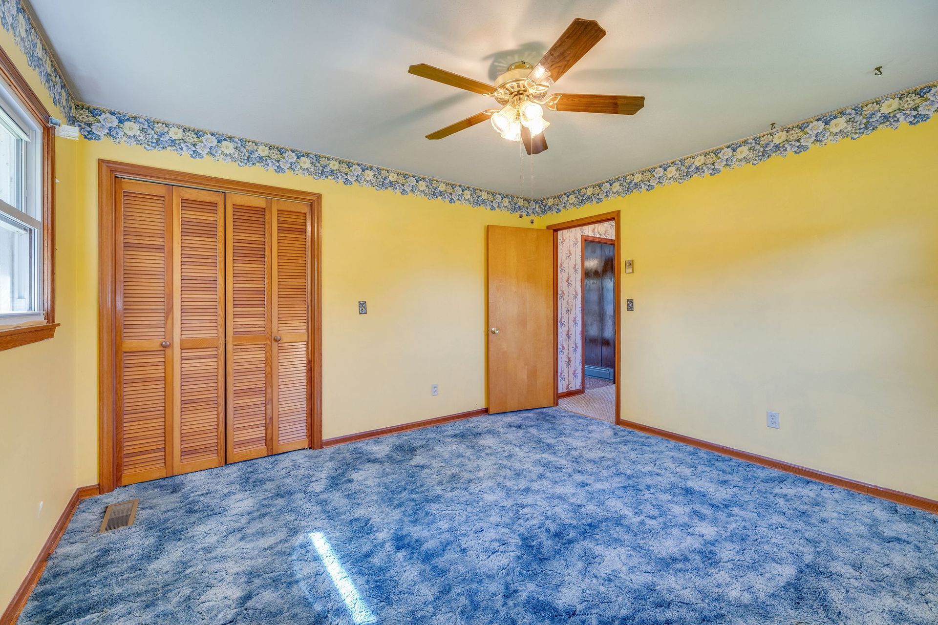 Empty bedroom with blue carpet, yellow walls, closet doors, and a ceiling fan with lights.