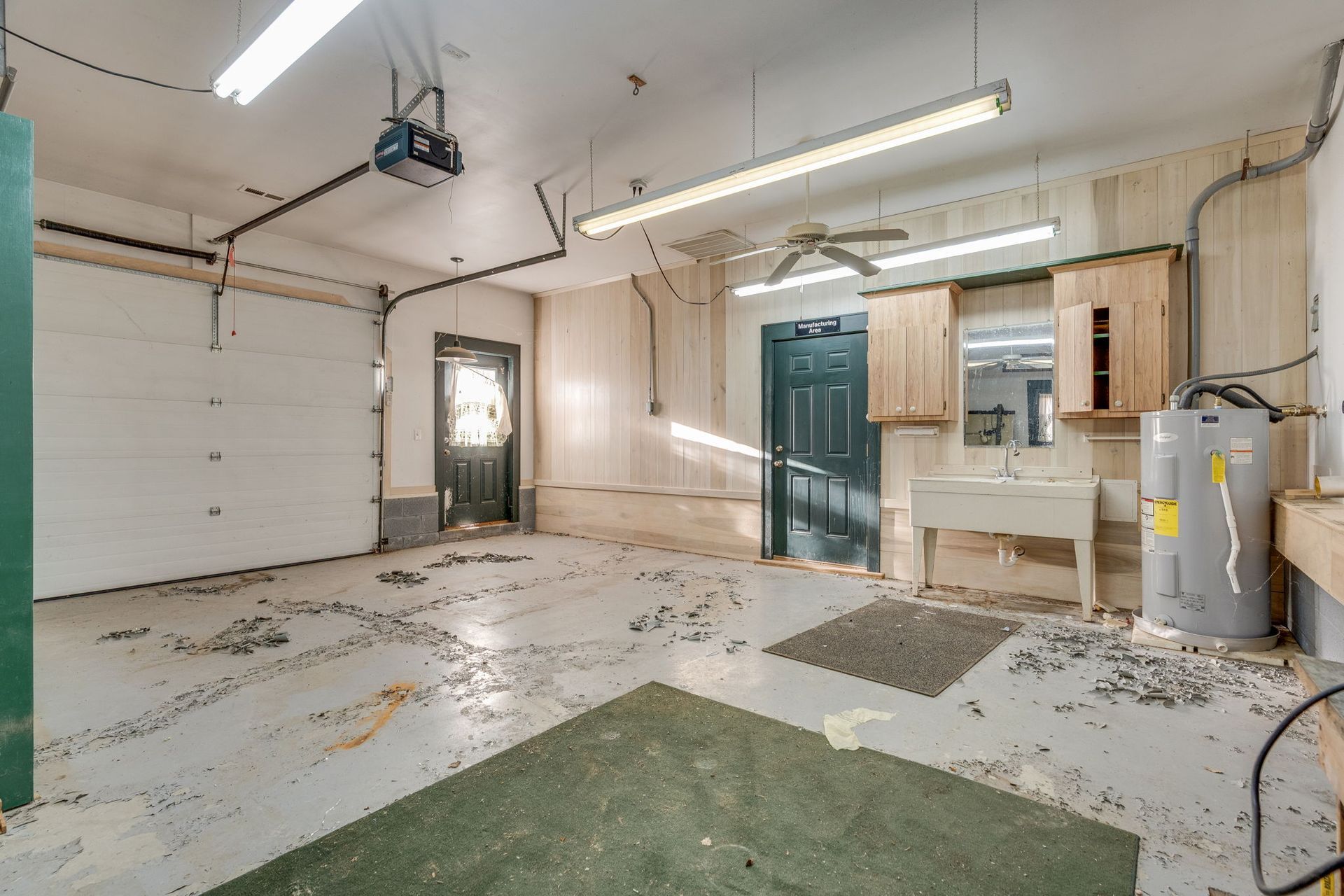 A messy garage interior with a closed garage door and a green floor square.