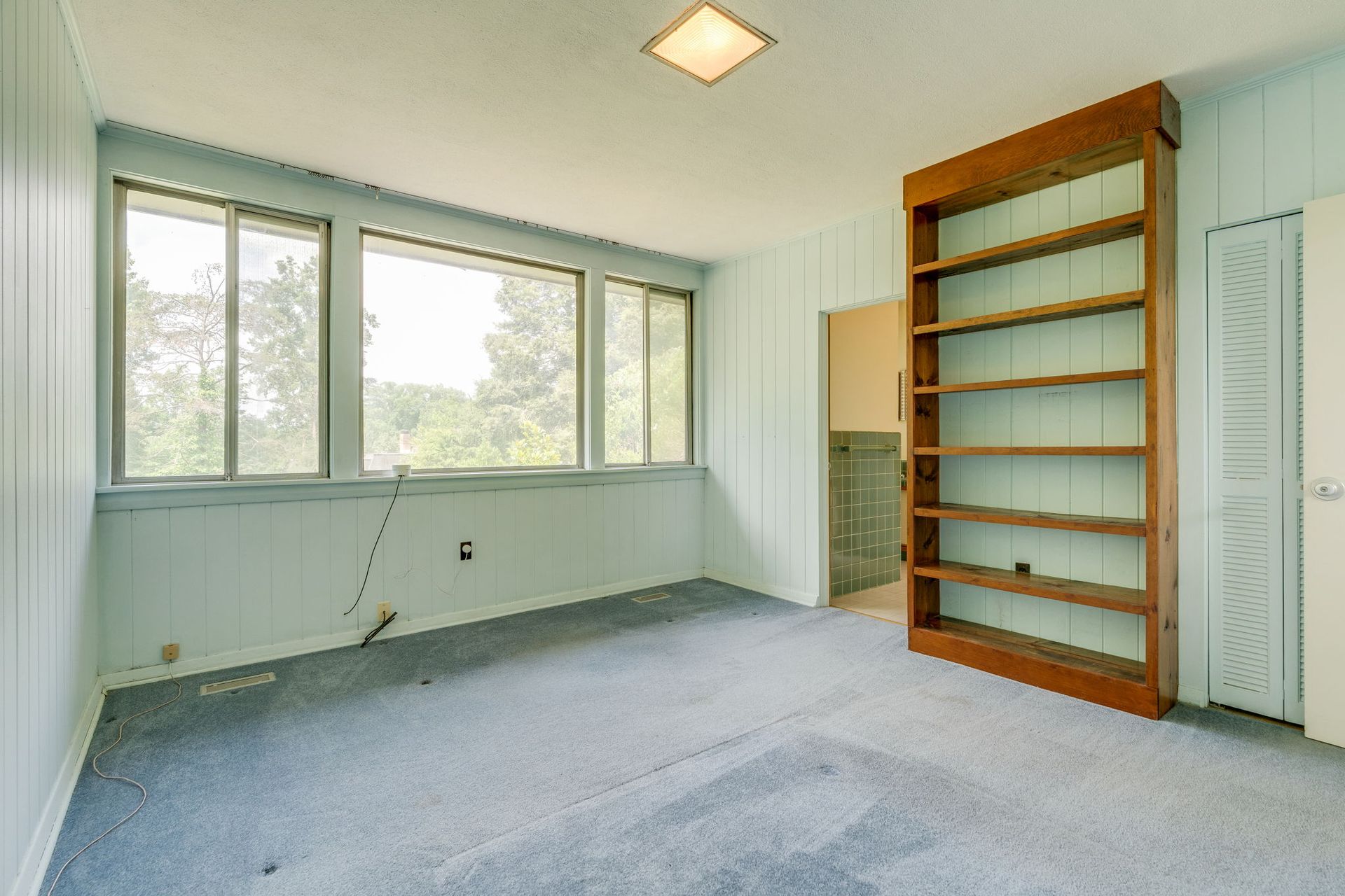 Empty carpeted room with large windows, built-in shelves, and a ceiling light