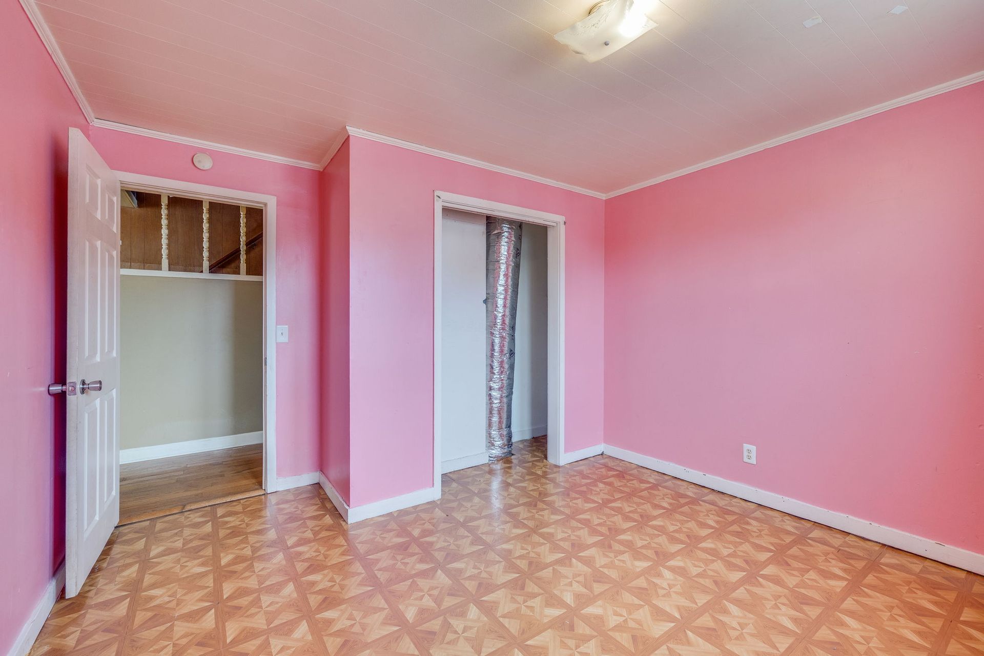 Empty pink bedroom with patterned wood floor and open closet door