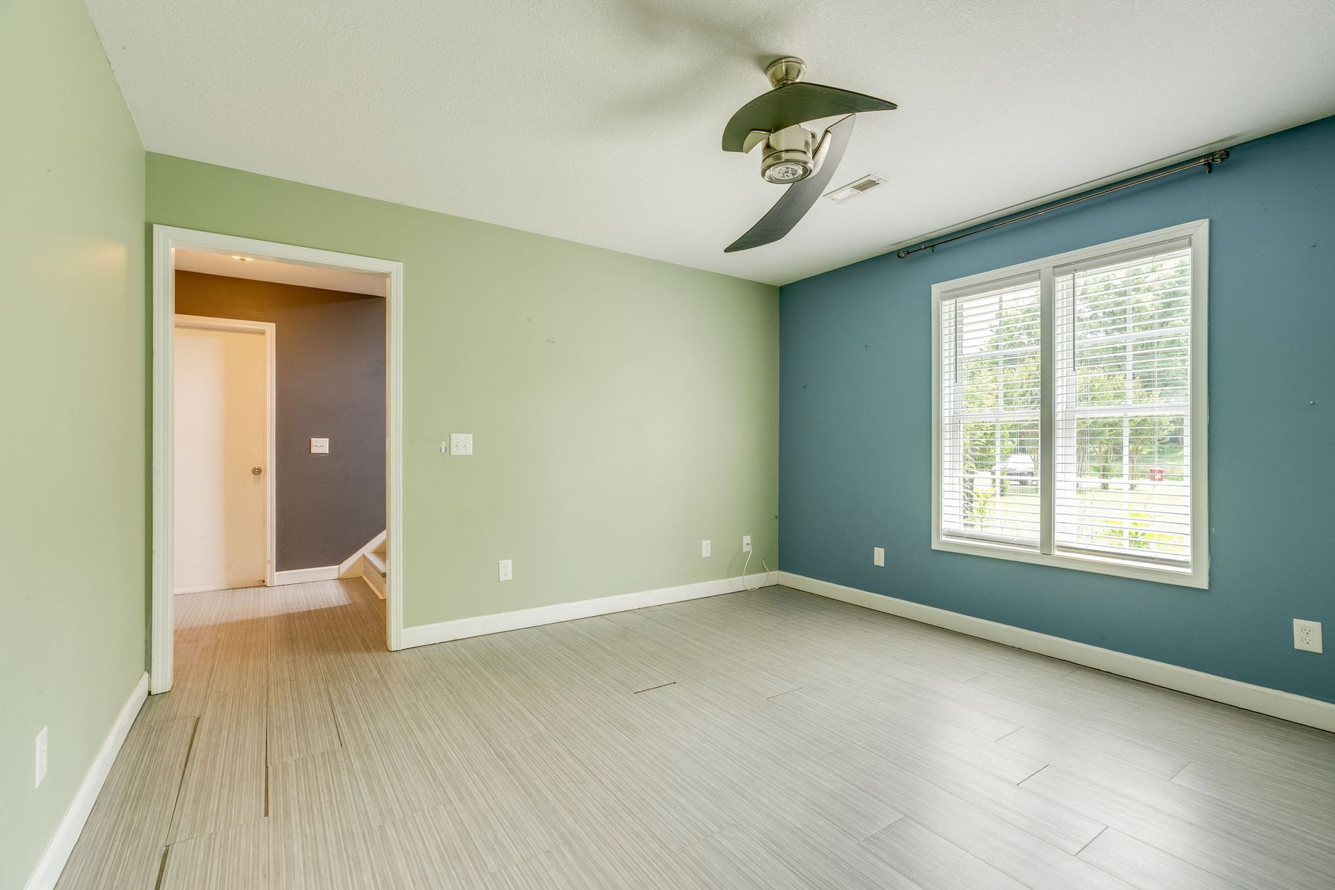 Empty room with mint green walls, teal accent wall, white blinds, and wood flooring.