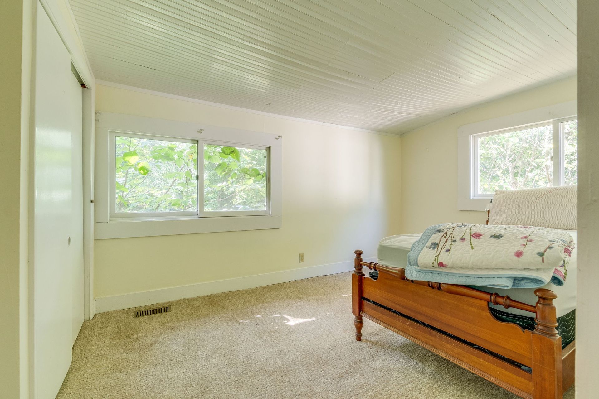 Bright bedroom with beige carpet, twin wooden bed, and large windows letting in daylight