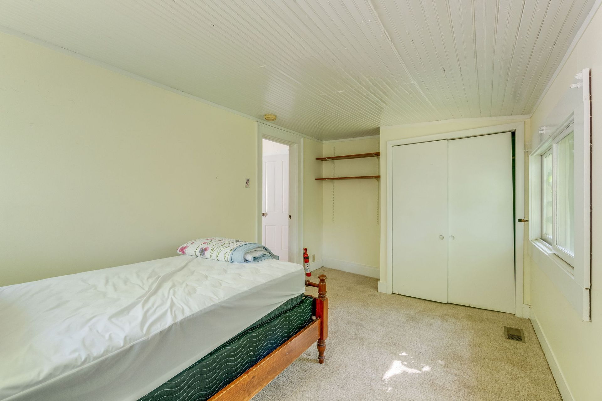 Small bedroom with a single bed, white closet doors, and a window on the right.