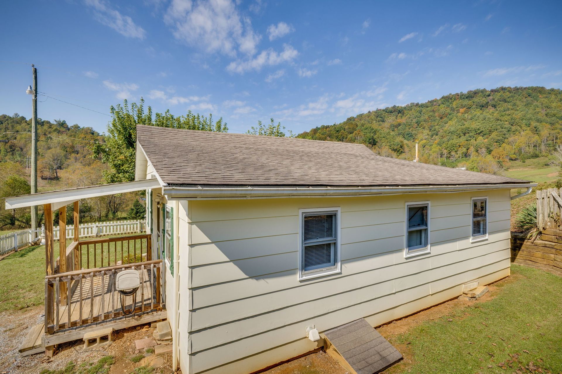Small beige house with a porch and blue windows on a hillside under a clear sky