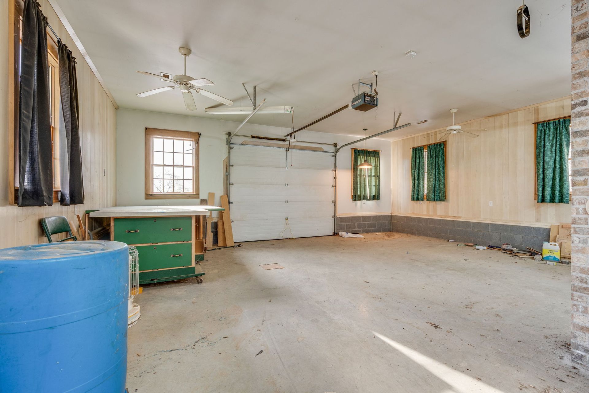 Empty garage interior with a closed white garage door, work bench, and blue barrel.