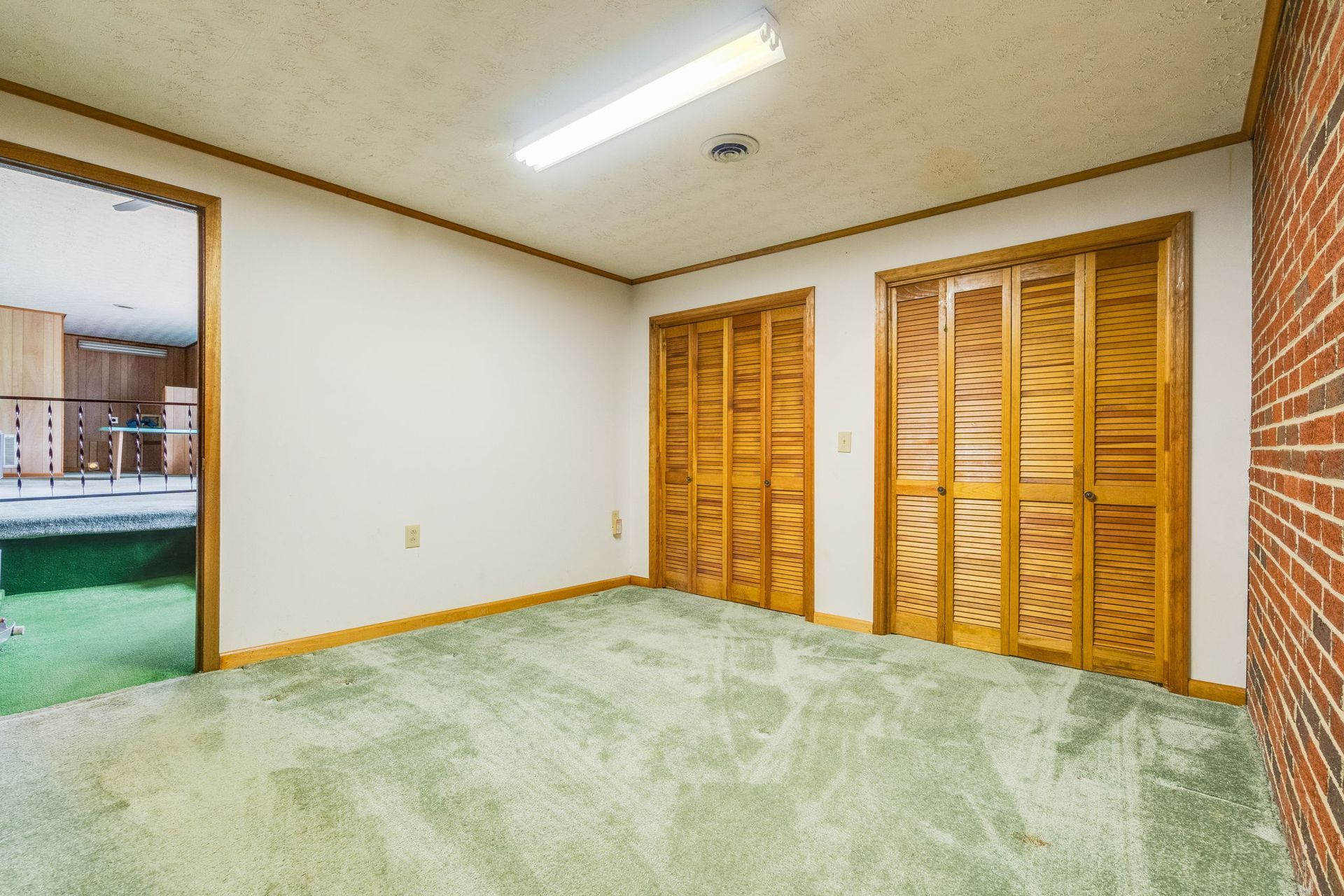 Empty room with green carpet, white walls, wood closet doors, and a brick accent wall.