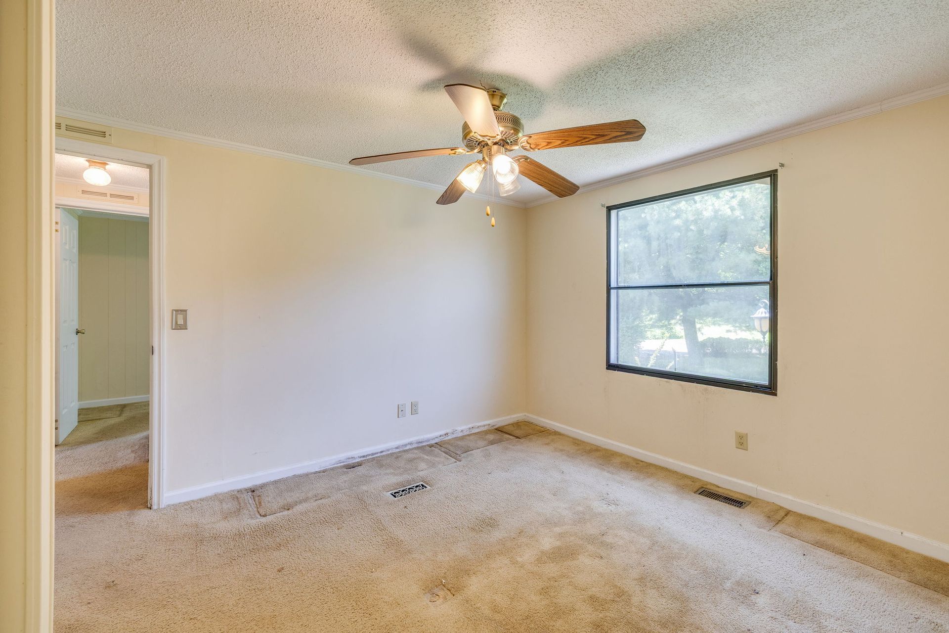 Empty beige bedroom with carpet, ceiling fan, and window letting in daylight