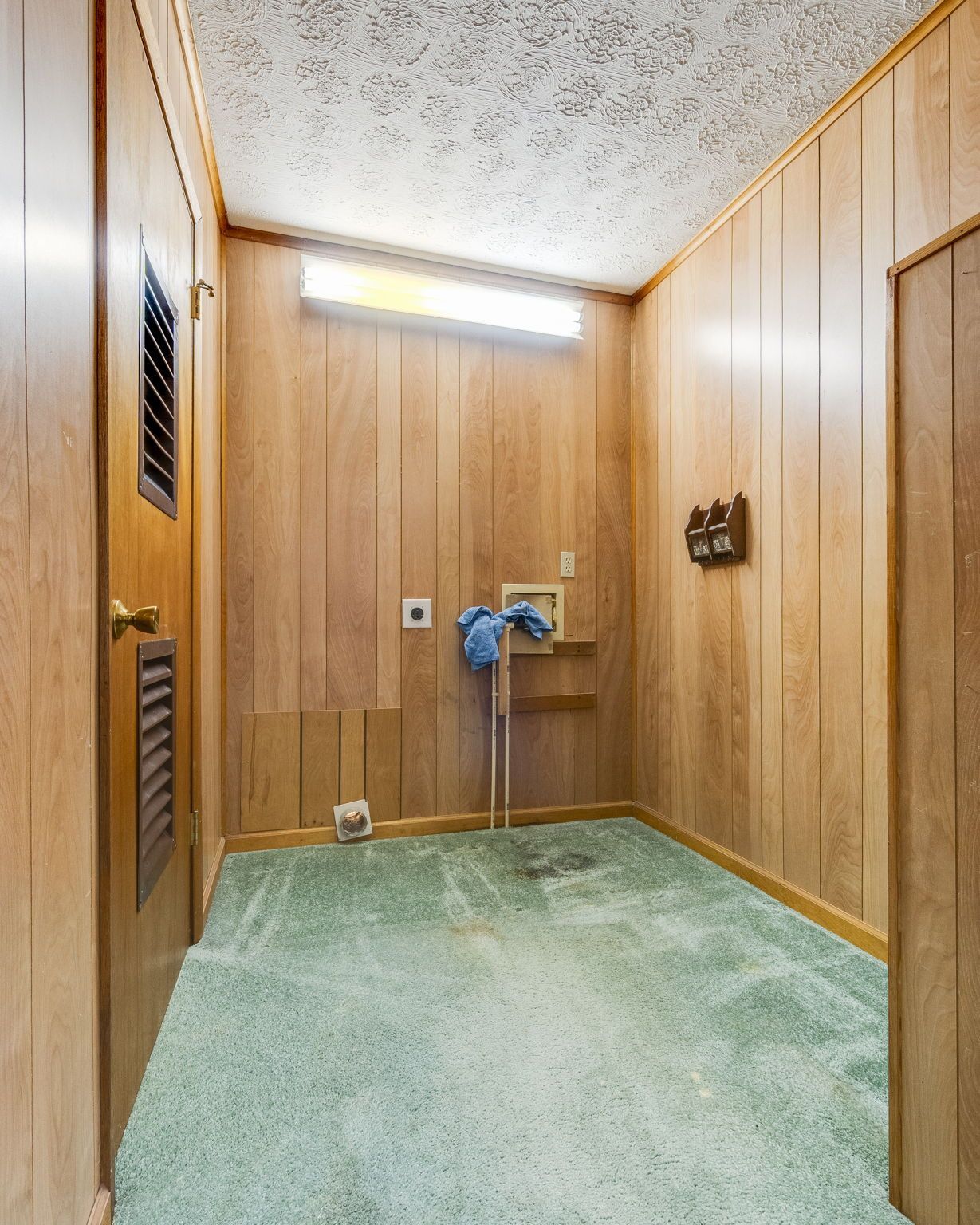 Wood-paneled laundry room with green carpet, utility sink, and wall vents