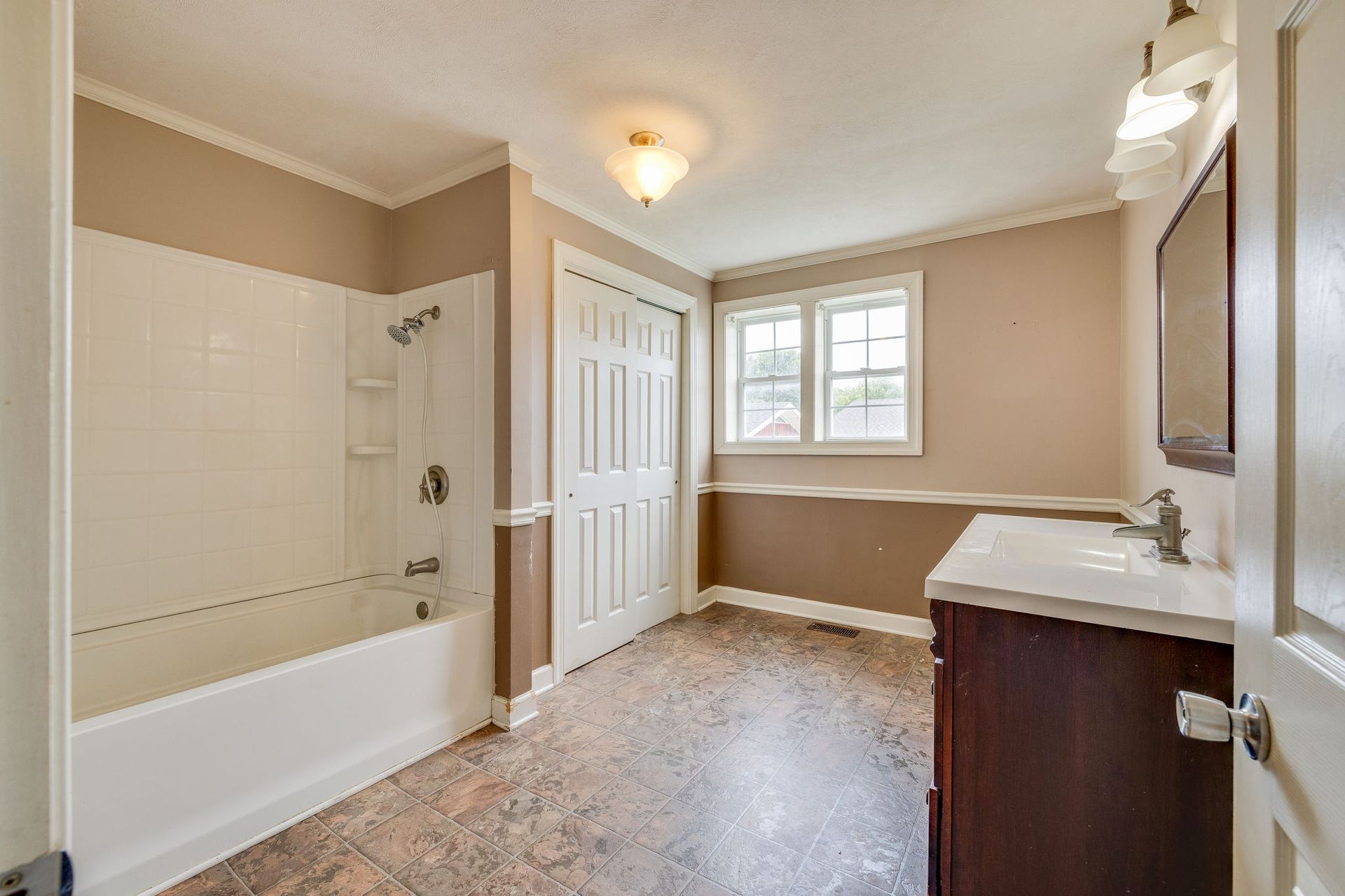Bright bathroom with a white tub, beige walls, window, and vanity.
