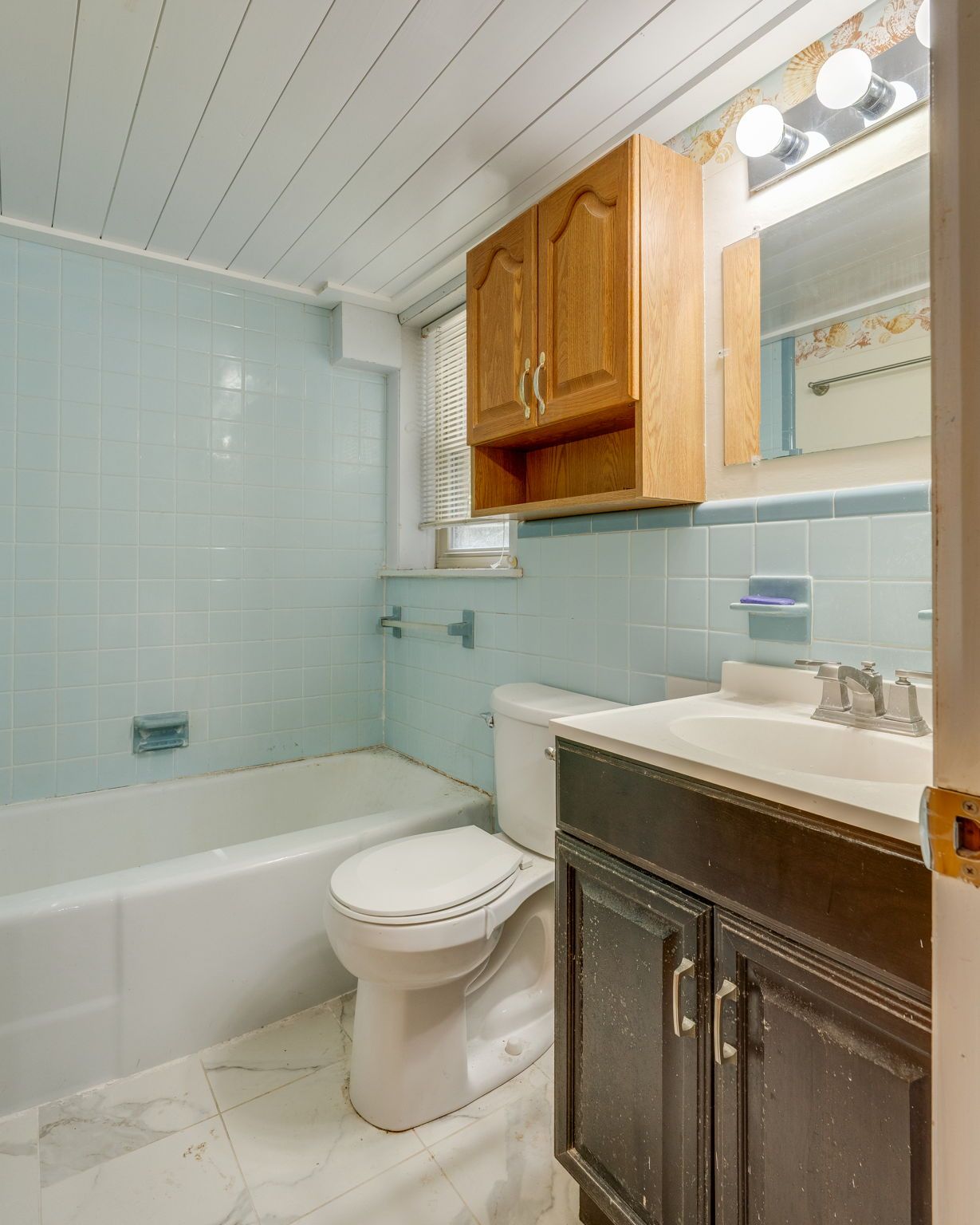 Small bathroom with white tub, light blue tile, dark vanity, and wooden wall cabinet.
