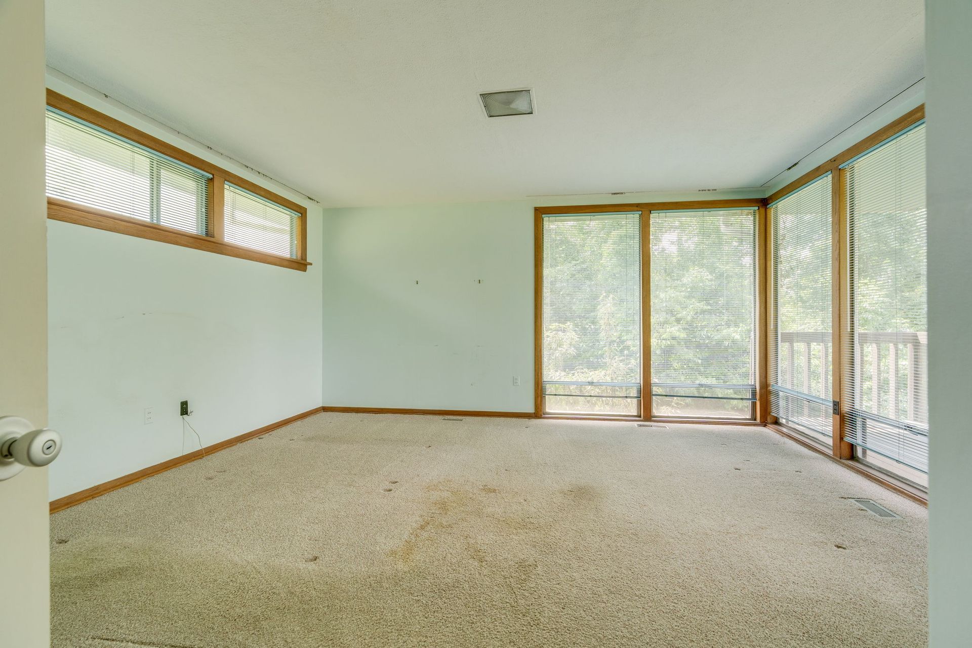 Empty carpeted sunroom with large windows and sliding glass doors overlooking trees