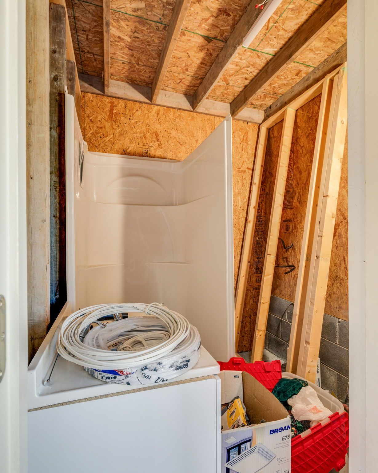 Partially finished bathroom with exposed studs, shower stall, and supplies stacked on a white appliance