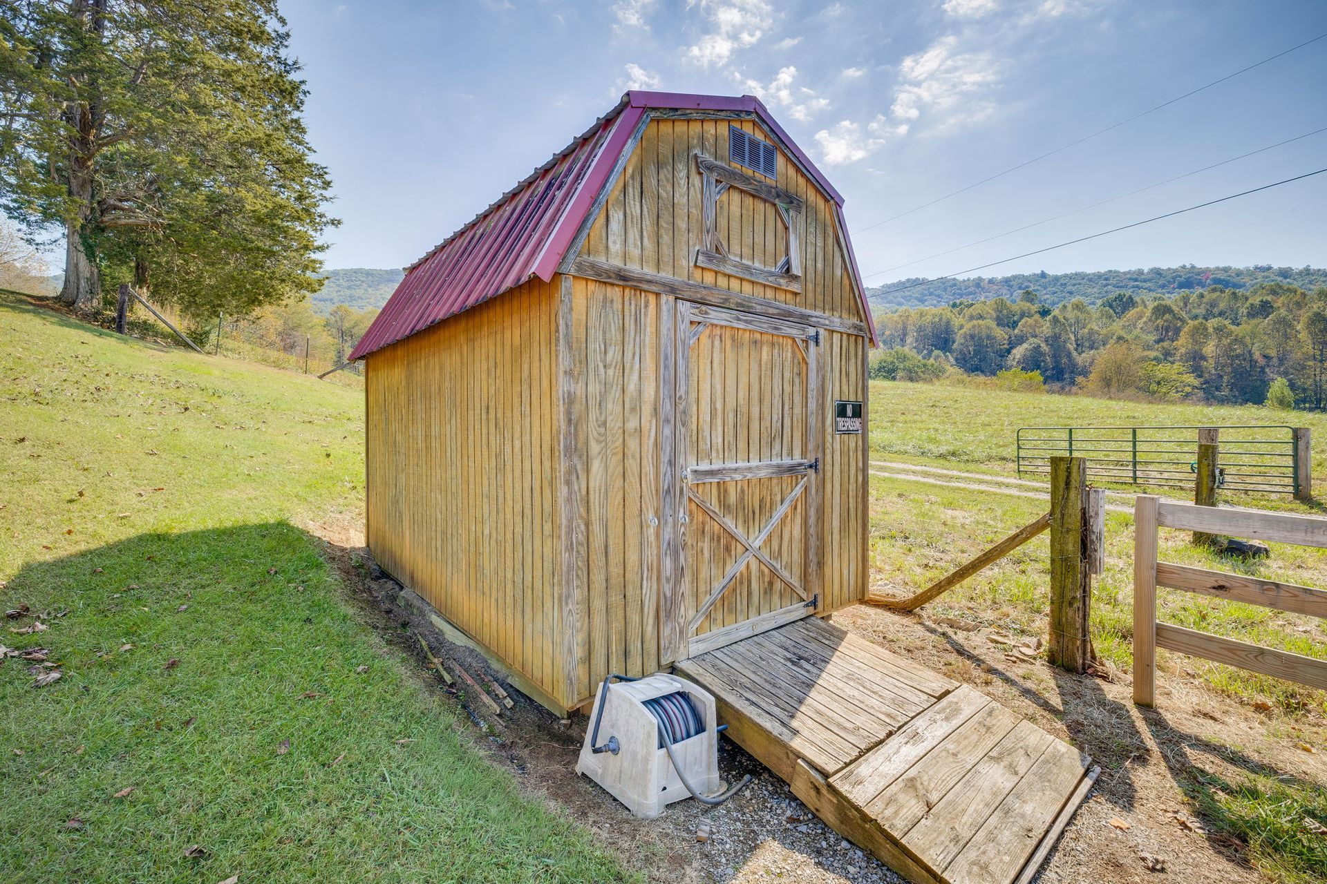 Wooden garden shed with red roof on a grassy hillside overlooking fields and hills